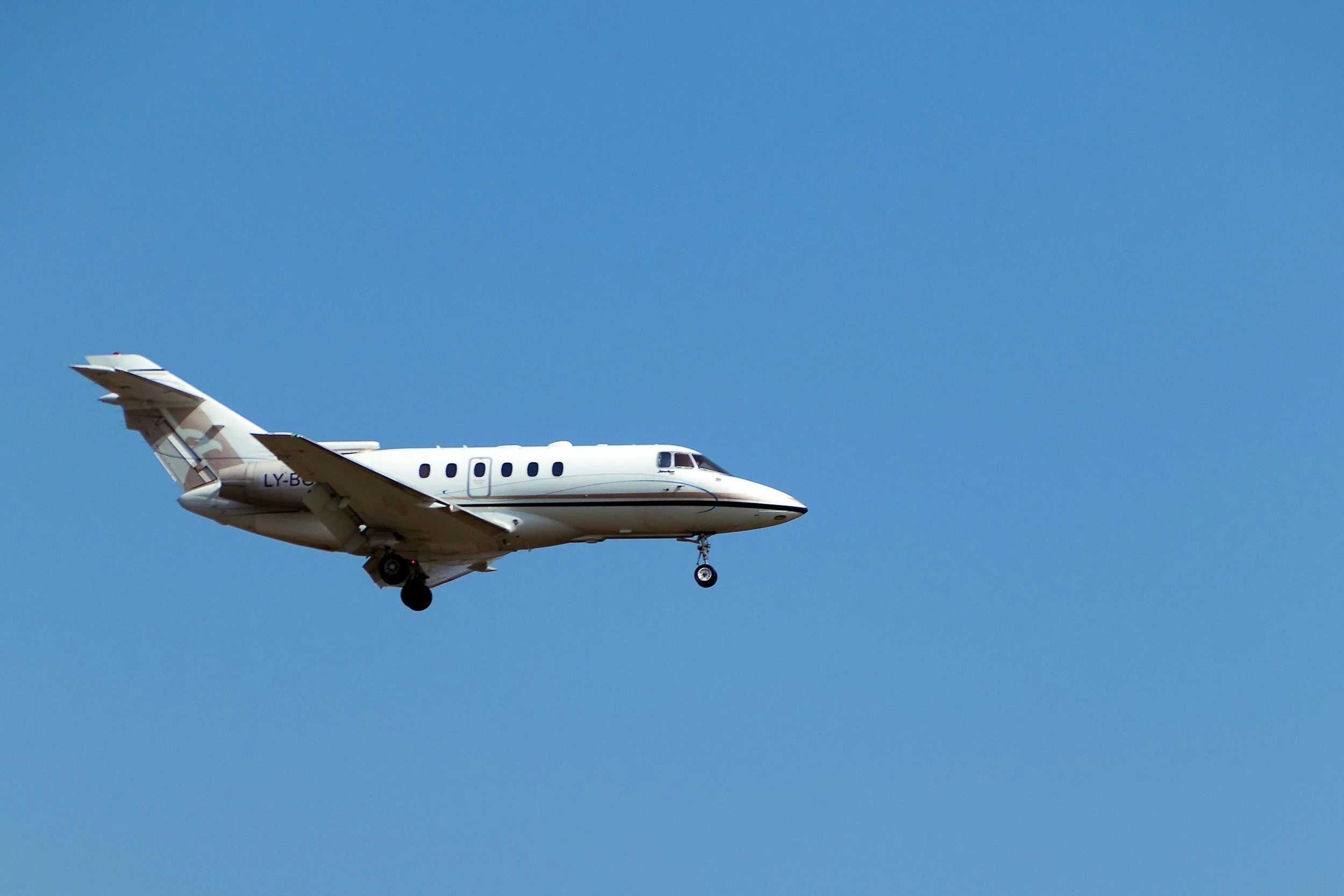 A white private jet airplane flying in a clear blue sky.