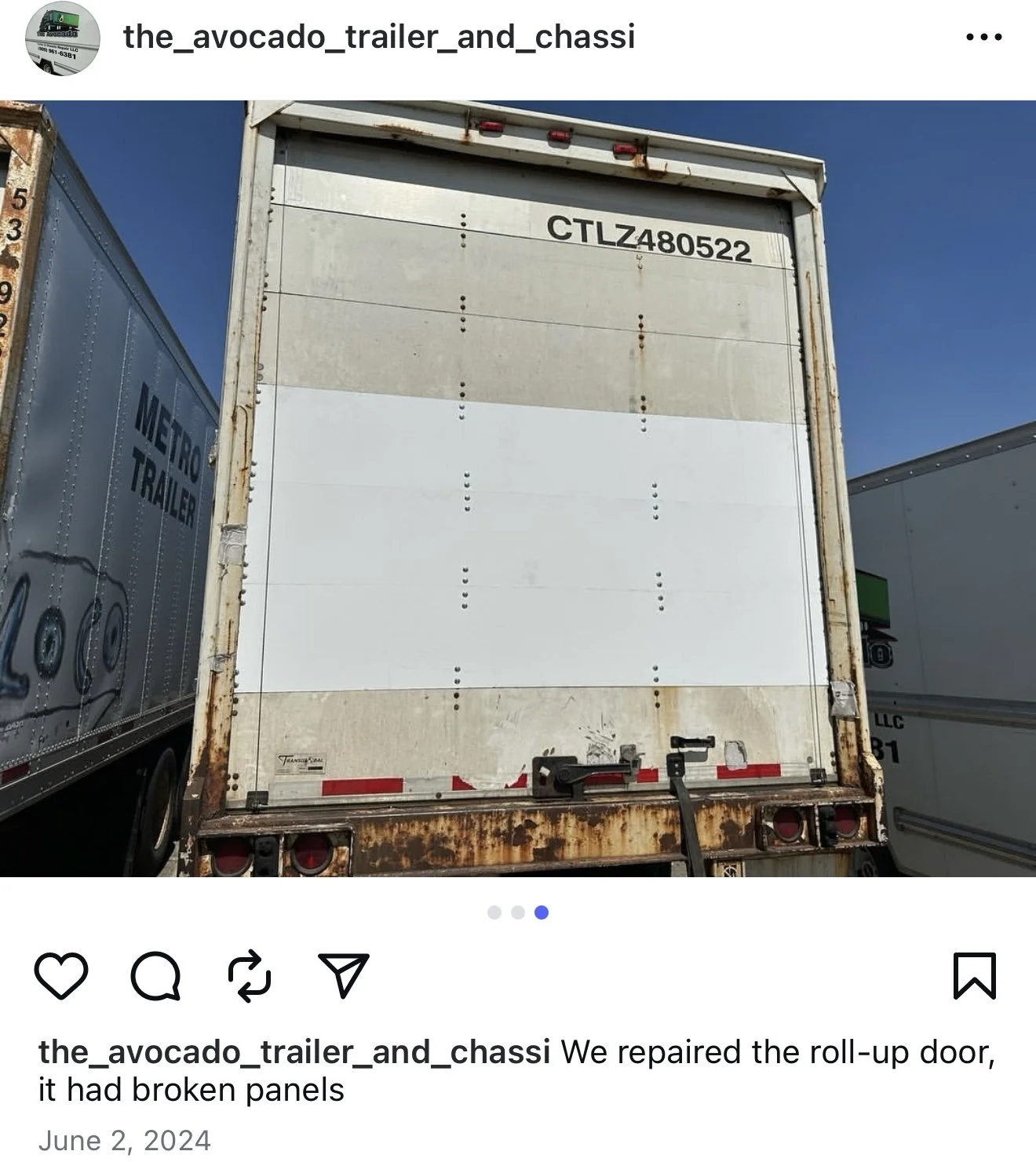 The back of a semi-trailer truck with a section of its roll-up door visible, showing broken panels. The trailer is parked between other trailers, one of which has a metal surface with lettering 'Metro Trailer.'