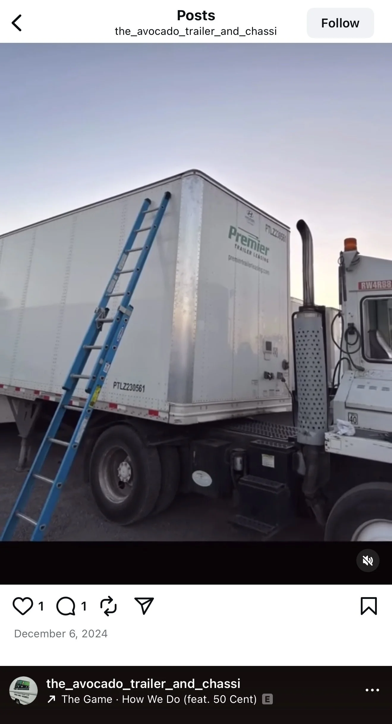 A white semi-truck trailer with a blue ladder leaning against it, parked next to the cab of the truck. The trailer has company branding and a website, and the sky is clear with no clouds visible.