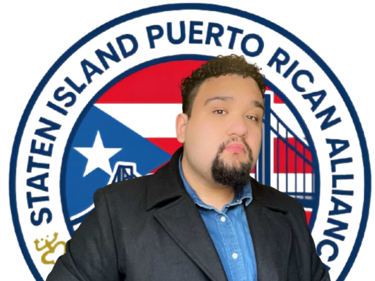 A man in a black jacket and blue shirt stands in front of the Puerto Rican flag and the State Island Puerto Rican Alliance logo.