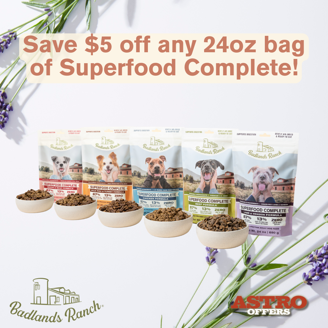 A promotional advertisement for Badlands Ranch dog food, featuring five different varieties of superfood complete dog food bags with images of dogs on the packaging, and five bowls of dog food in front of them. The text reads, 'Save $5 off any 24oz bag of Superfood Complete!' with purple lavender flowers and green leaves in the background.