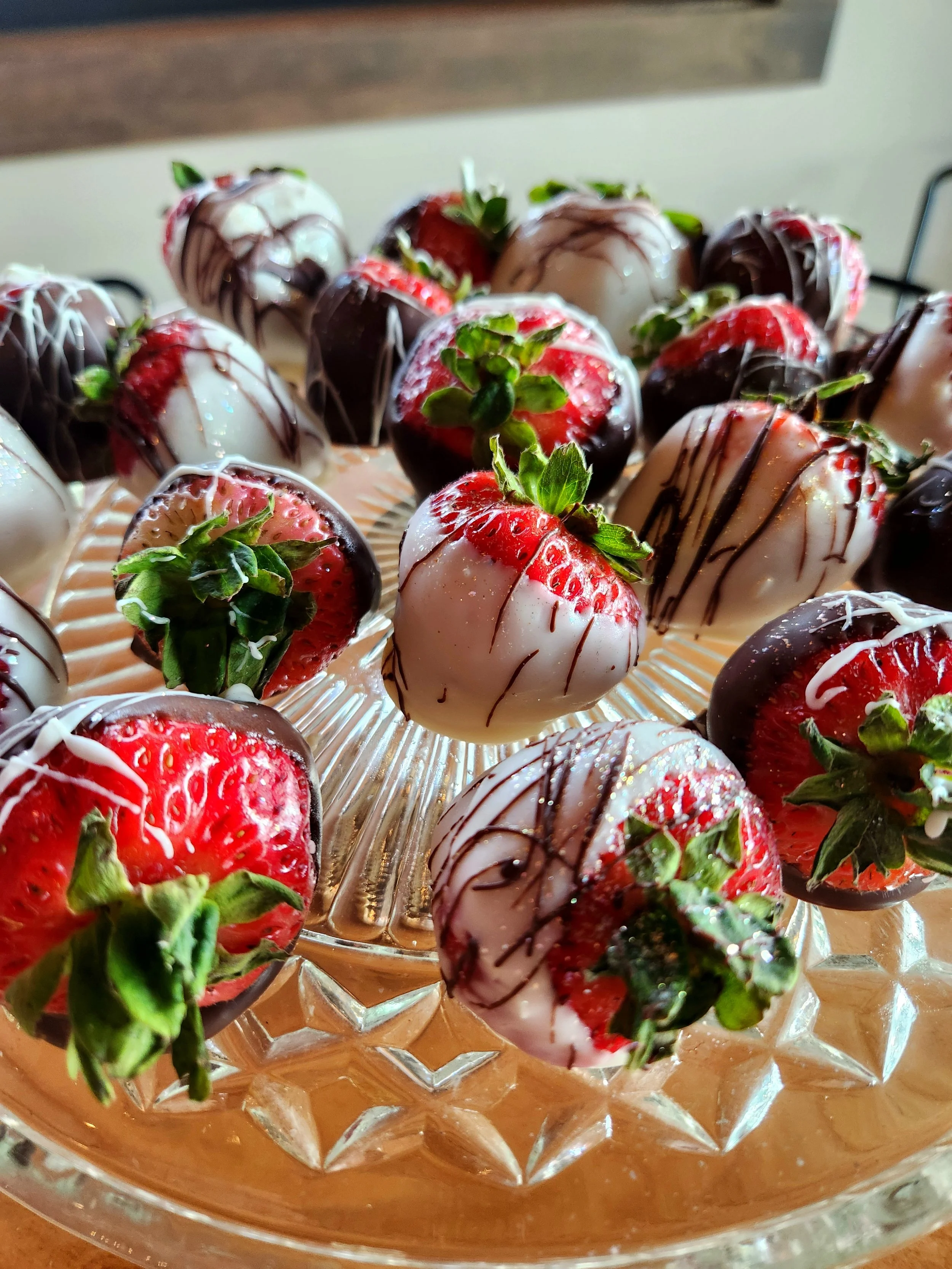 Strawberries dipped in dark and white chocolate, decorated with white and dark chocolate drizzle, arranged on a glass platter.