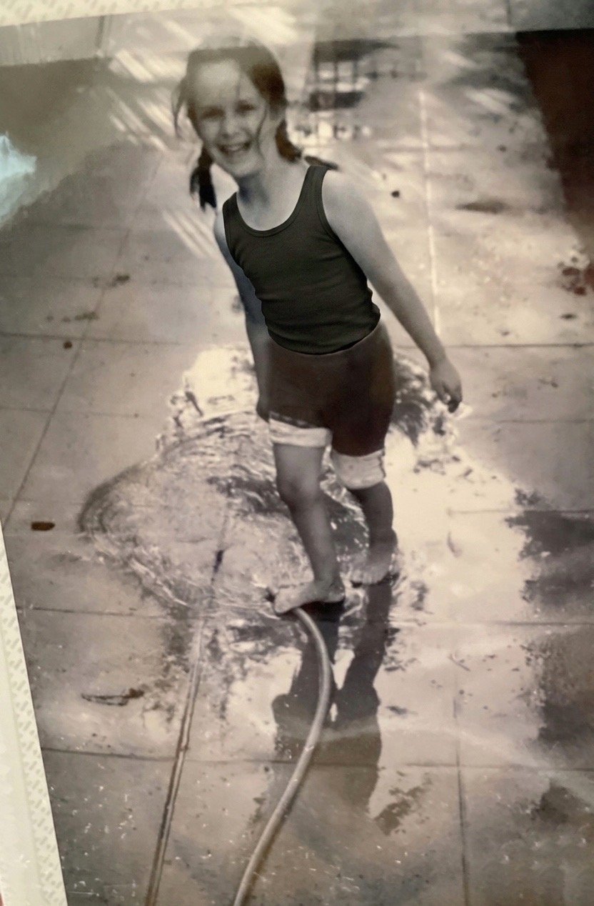 4 year old Eva Luna Ortiz appears with a garden hose smiling and playing on the concrete driveway of her home in 2004