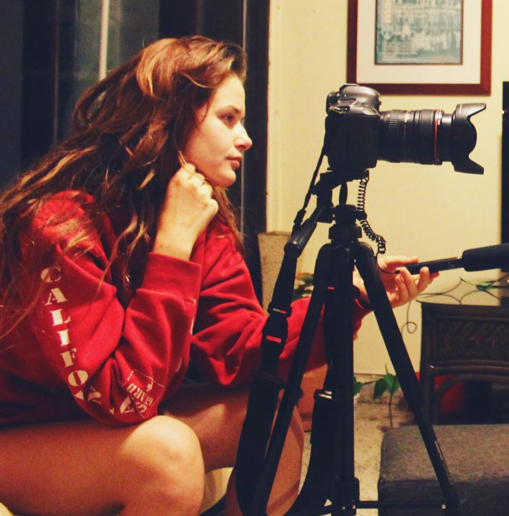 Eva Luna Ortiz sitting in front of her tripod filming with her DSLR and holding a microphone.