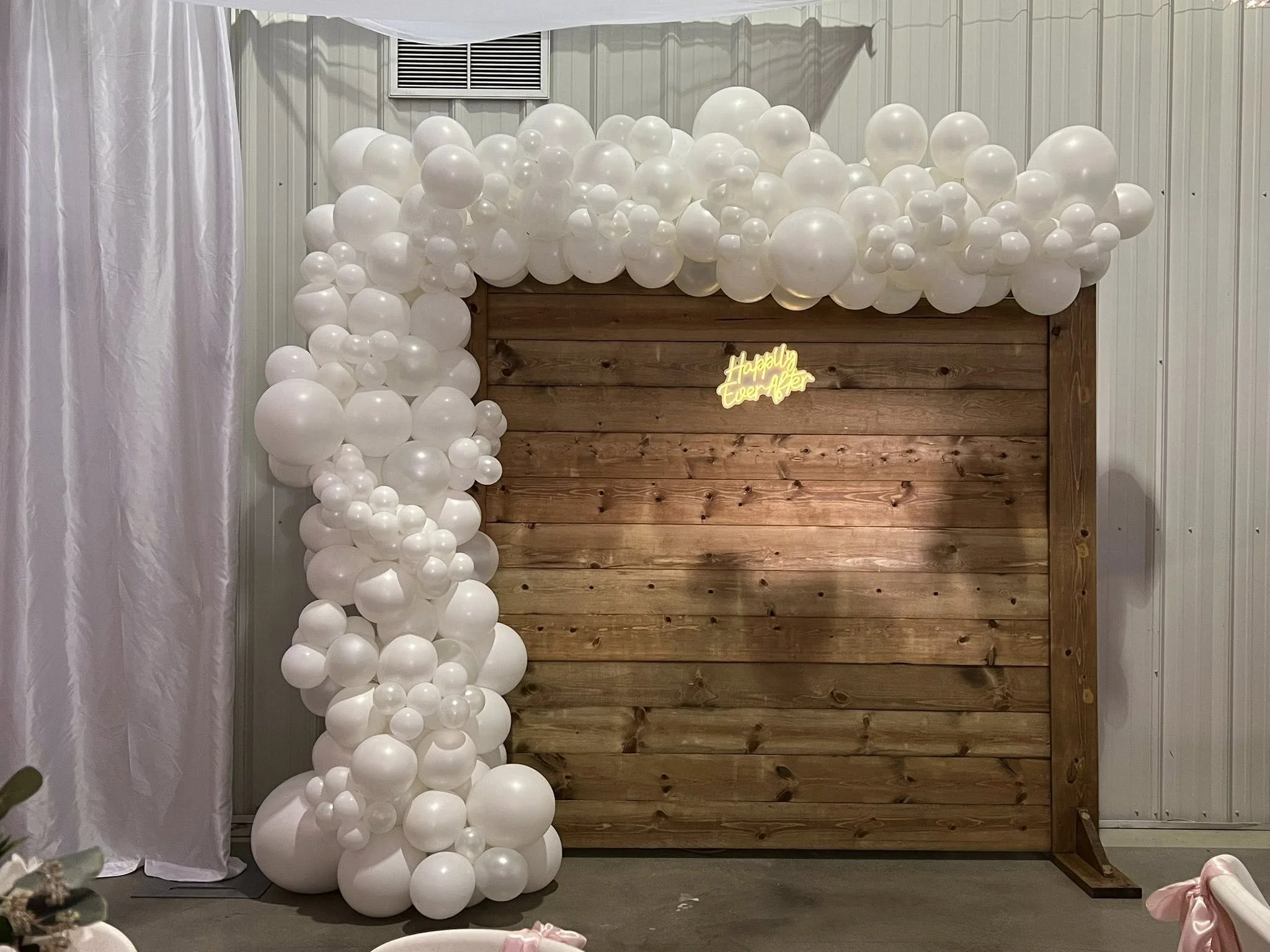 Wooden backdrop decorated with white balloons in various sizes and a neon sign that reads "Happily Ever After".