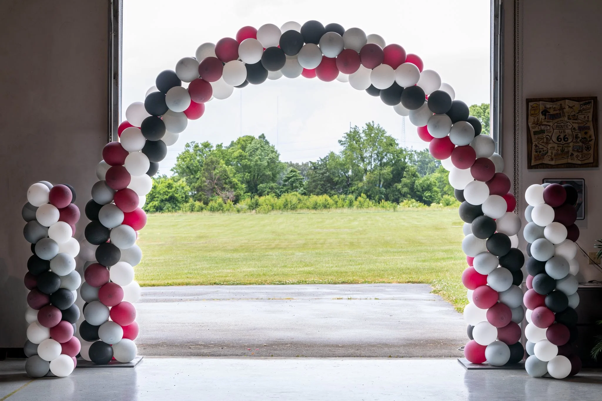 Balloon arch and columns at the entrance of a celebration venue with an outdoor view of green trees and grass.