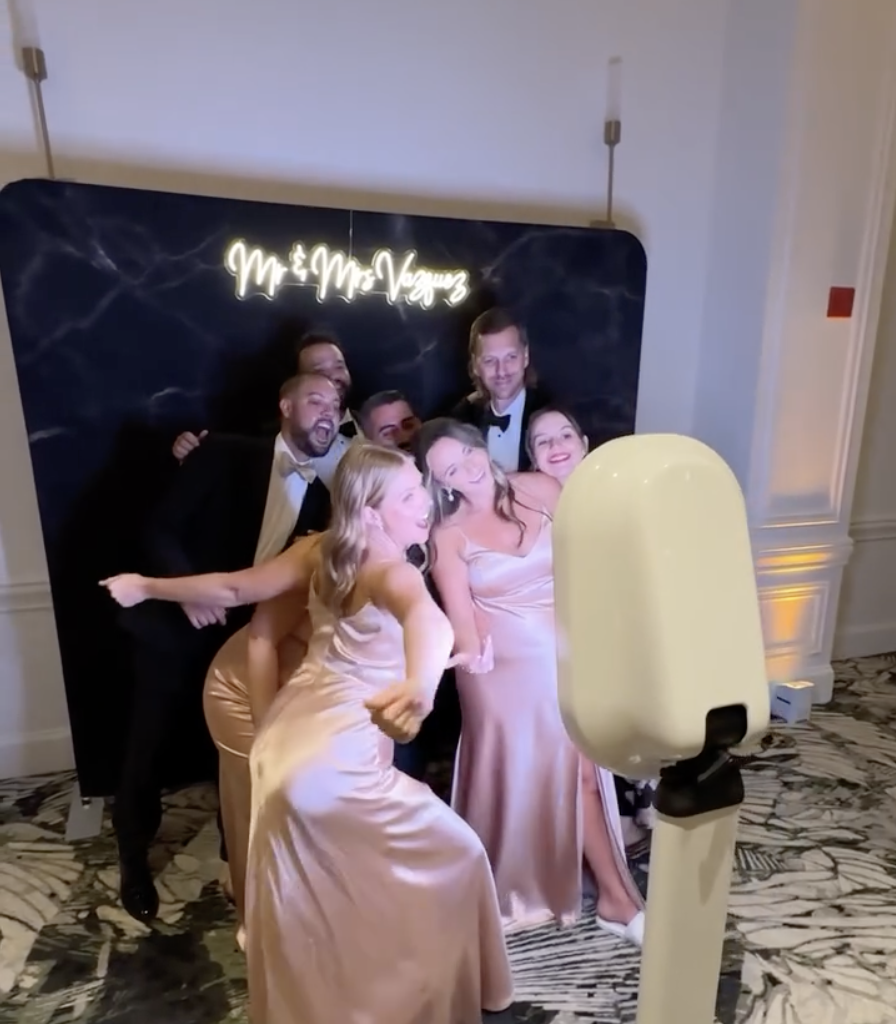 Wedding guests posing with props at Versamix Music’s luxury photo booth with a flower wall backdrop.