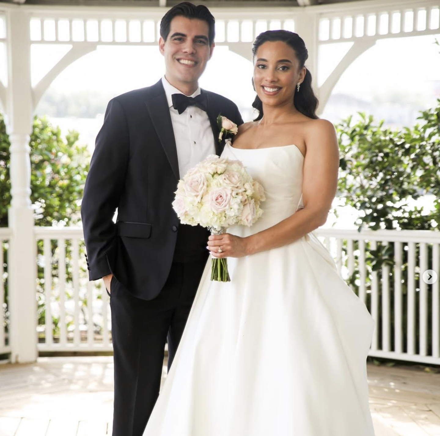 Bride and groom Vázquez smiling together in a gazebo on their Savannah wedding day, holding a bouquet of roses.