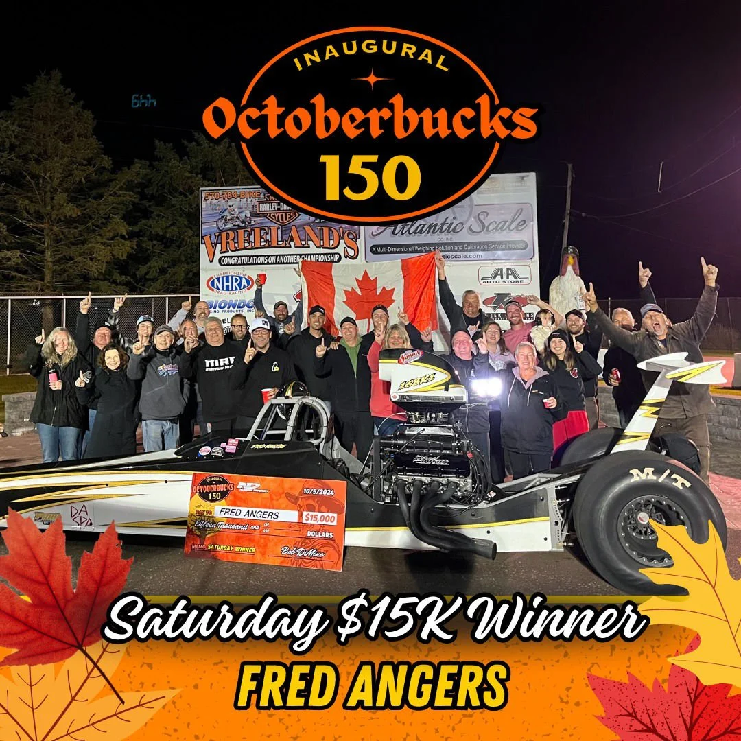 Group of people celebrating on a race track with a dragster, holding a Canadian flag, and a large check for $15,000. The event is the inaugural Octoberbucks 150, won by Fred Angers on Saturday. The background features banners and trees, with autumn l