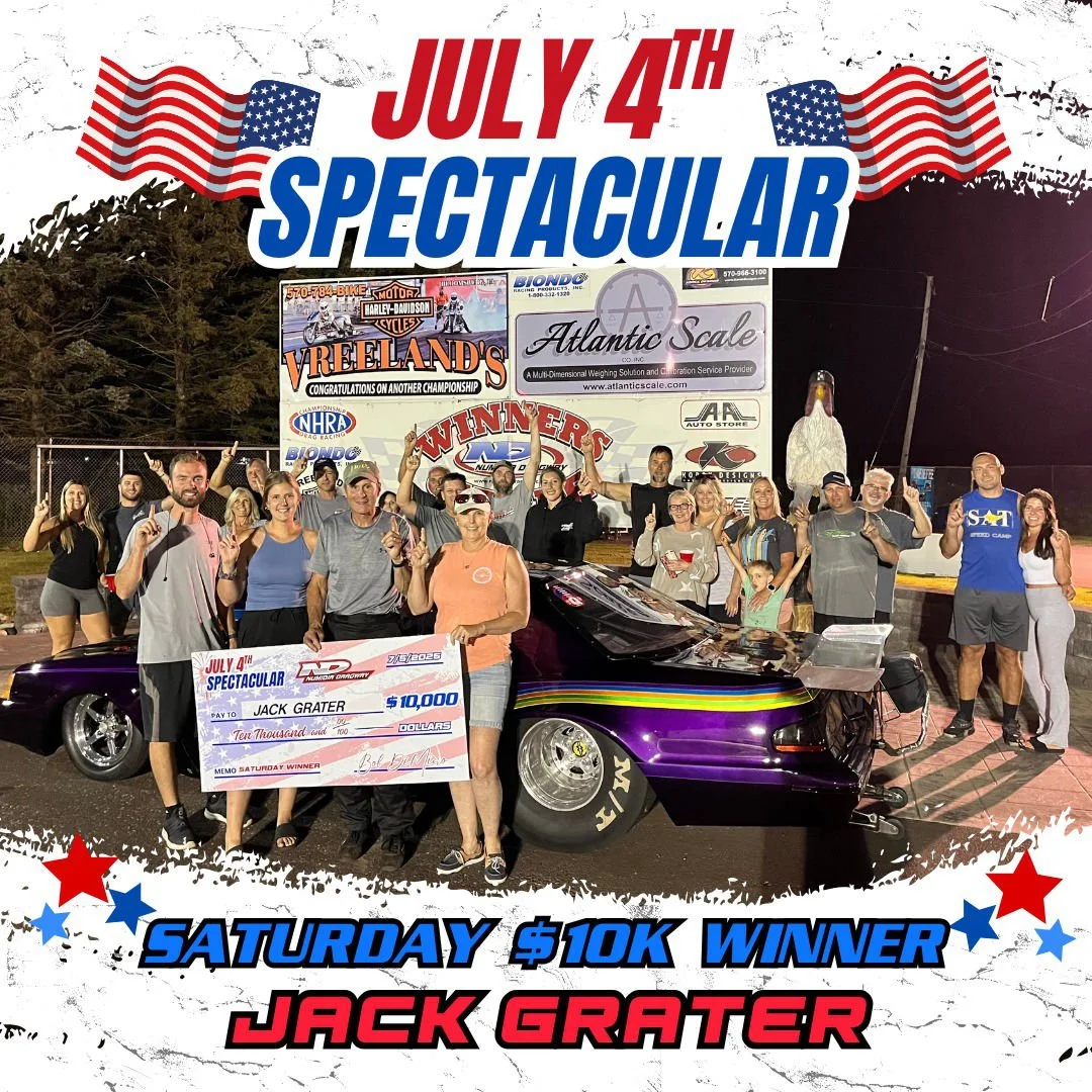 Group of people celebrating at a racing event with a race car, holding a large check for $10,000 awarded to Jack Grater, with American flags and event banners, the text 'July 4th Spectacular' and 'Saturday $10K Winner Jack Grater'.