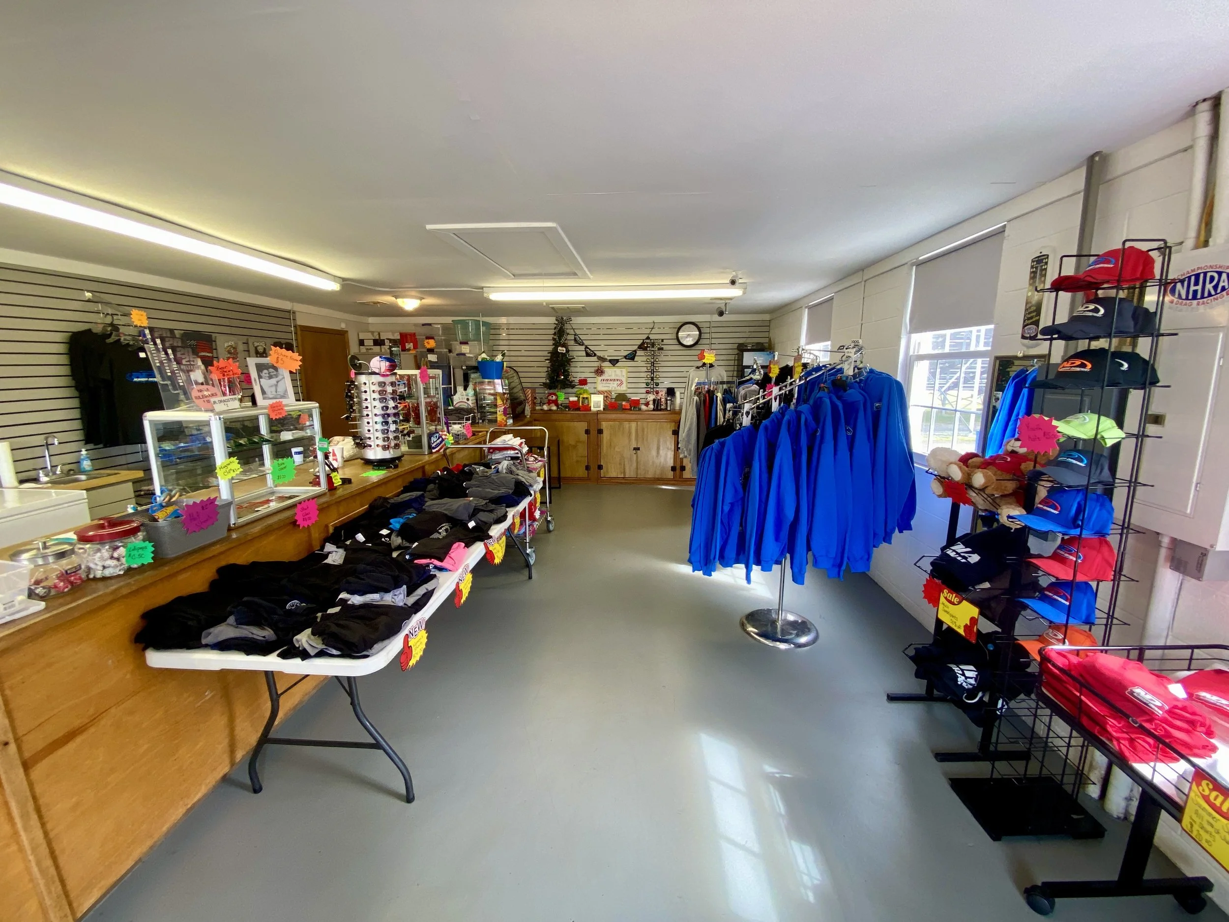 Indoor retail store with various clothing items, hats, and accessories on display, some with bright sale signs, and a counter in the background.