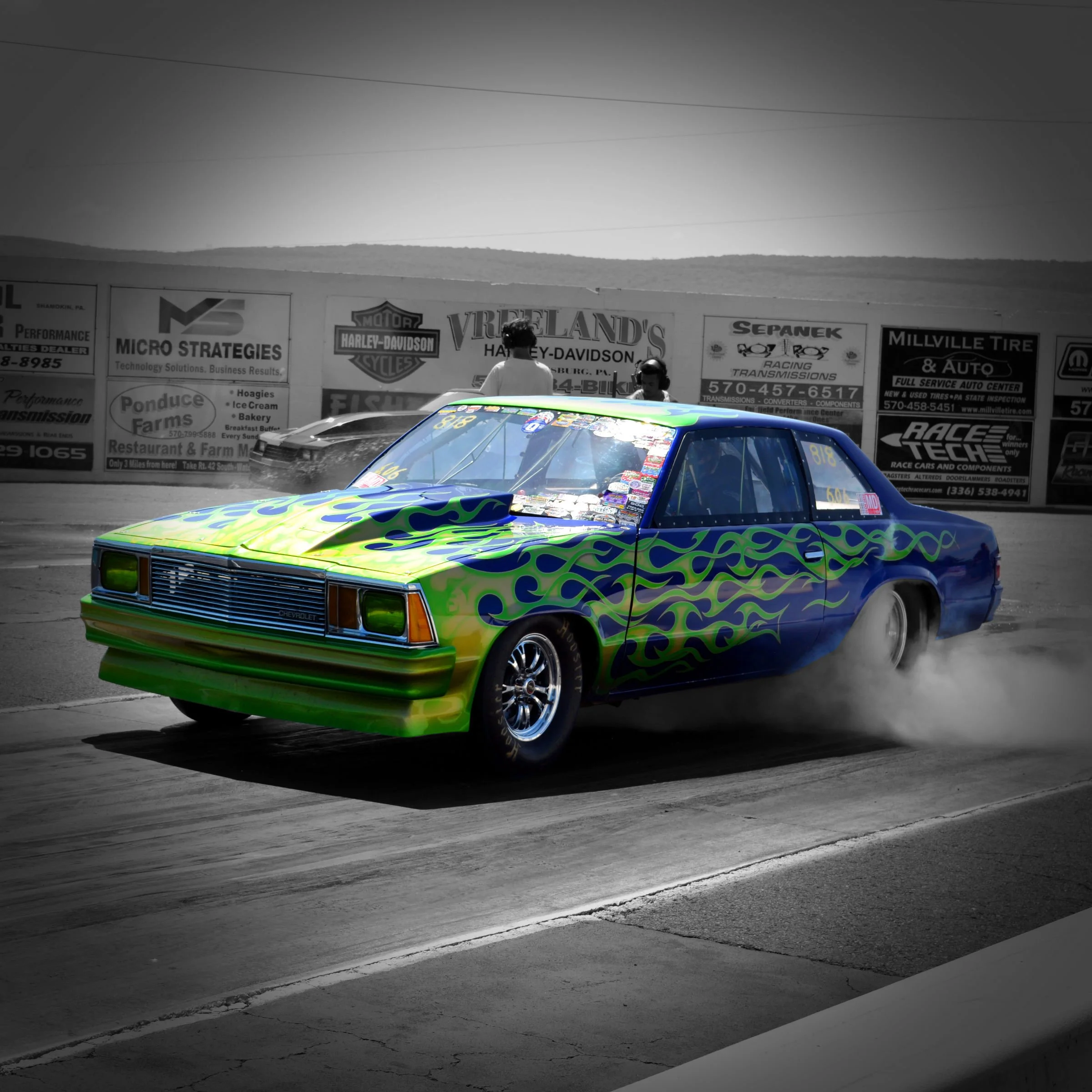 Colorful race car with green, blue, and yellow flames on a racetrack.