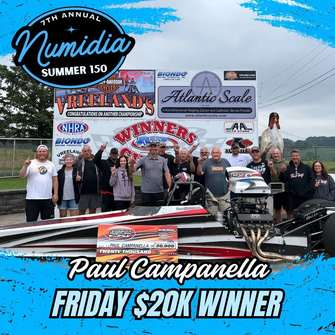 Group of people celebrating victory at a drag racing event, with a race car and a large check for $20,000, at the 7th annual NUmidia Summer 150 race.