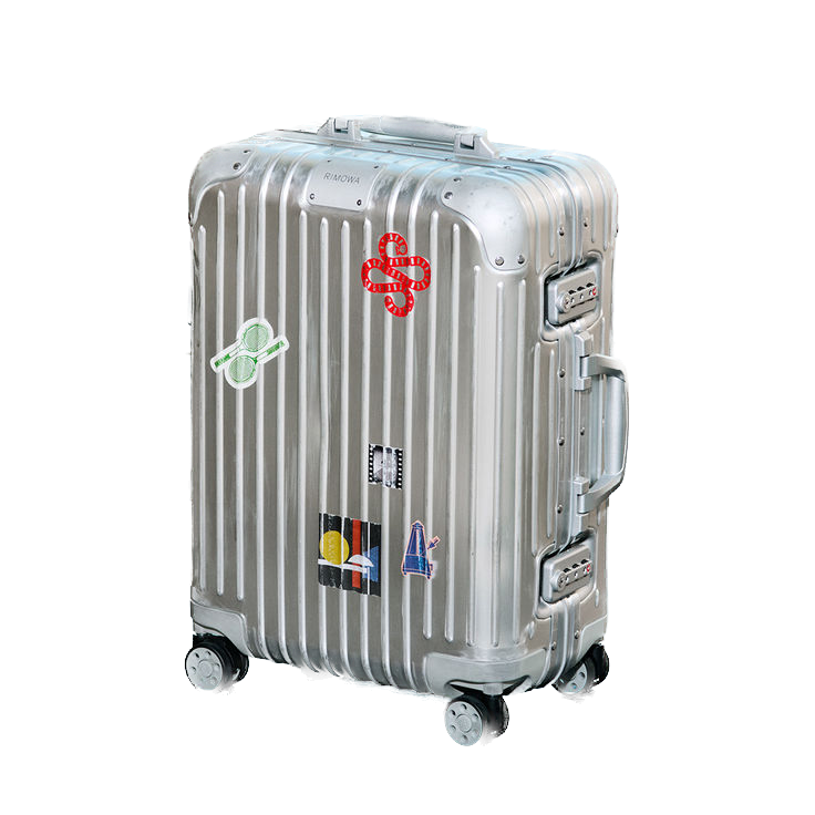 Silver hard-shell suitcase with stickers, including a red snake, green glasses, a yellow circle with three lines, and a small blue chair, on a black background.