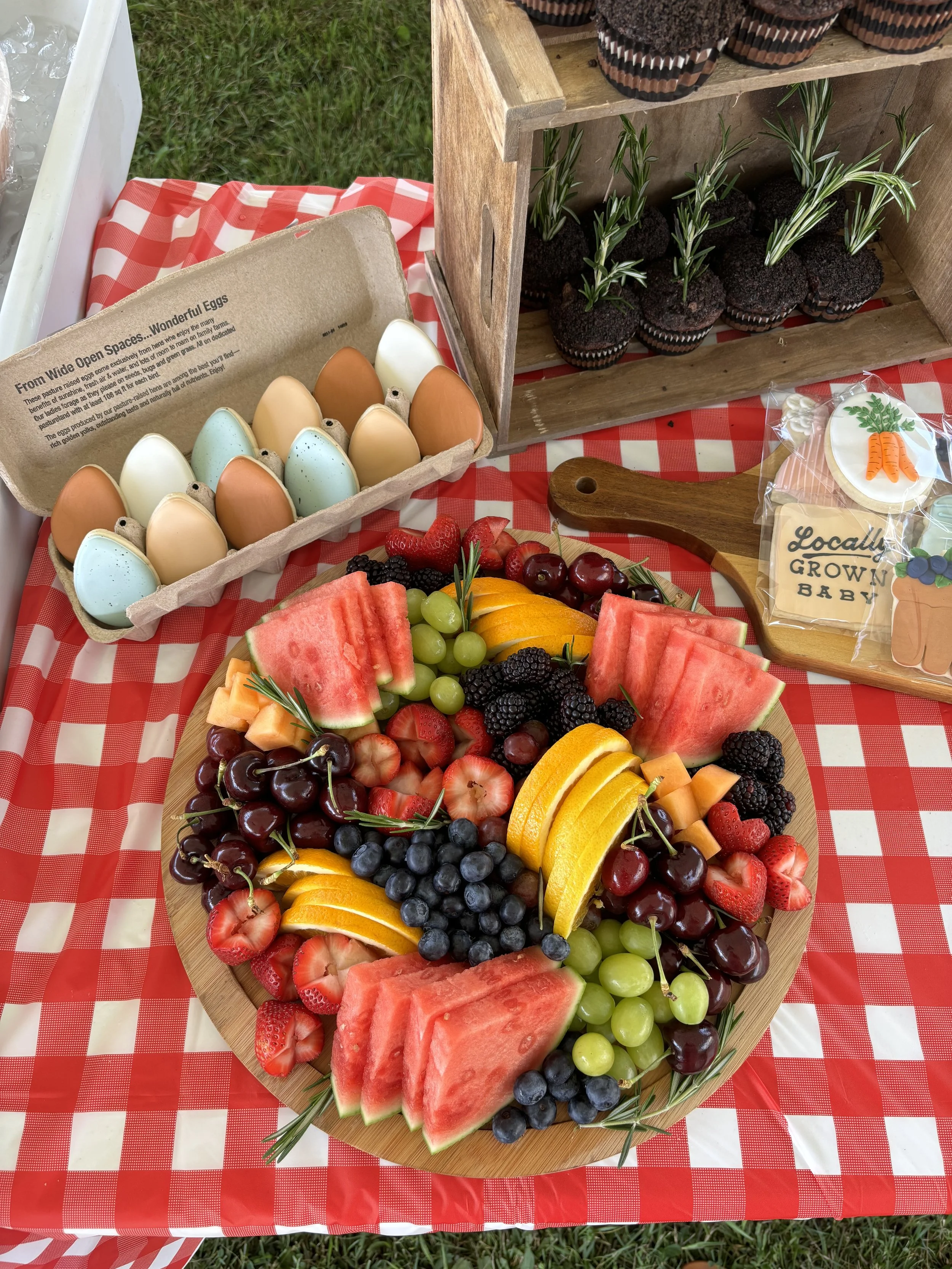 egg themed cookies, checkered picnic tablecloth, locally grown baby shower, fruit plate, cupcakes with plants sprouting, desert table