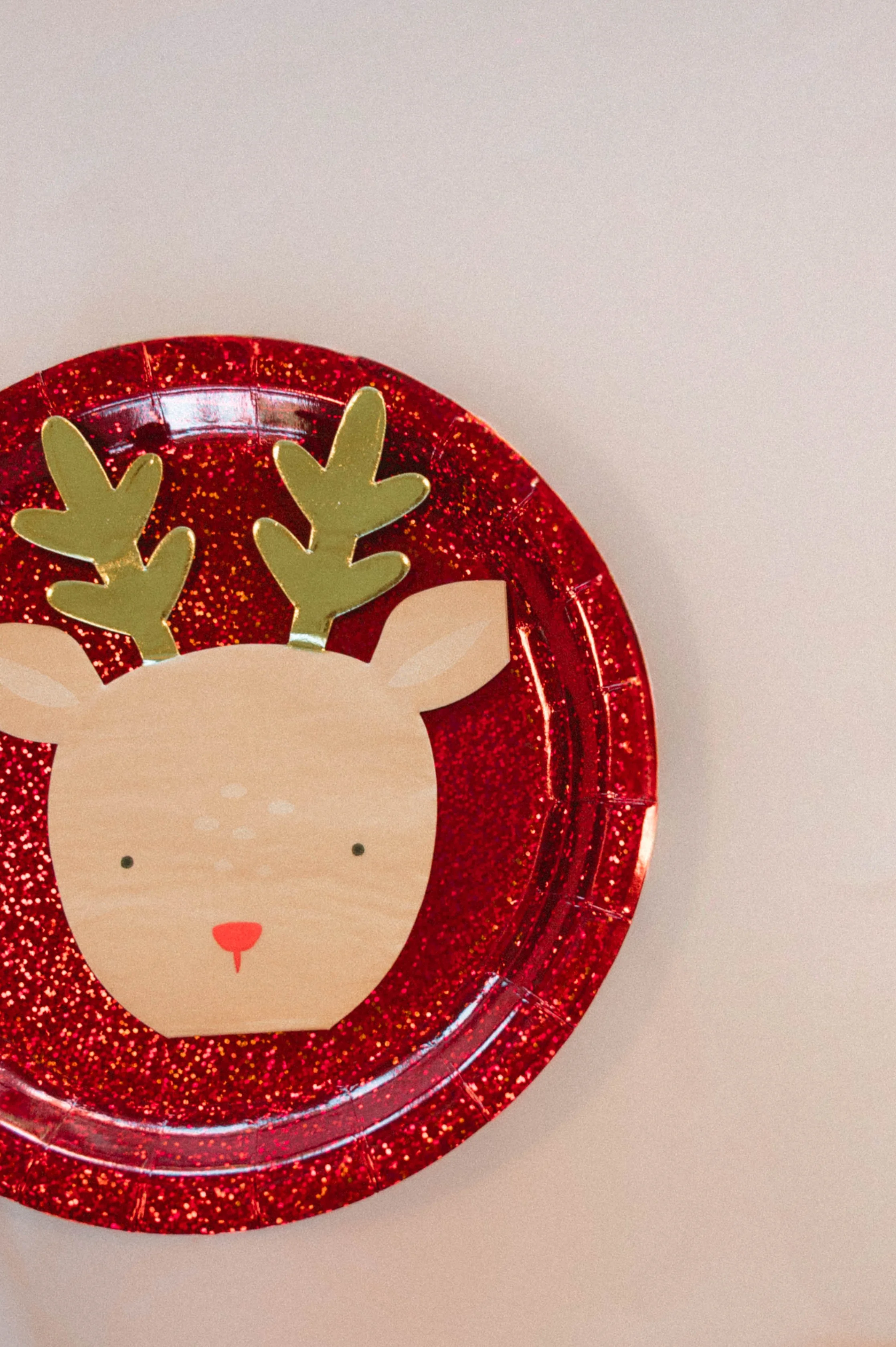 Red glitter Christmas decoration with a reindeer face and gold antlers on a white background.
