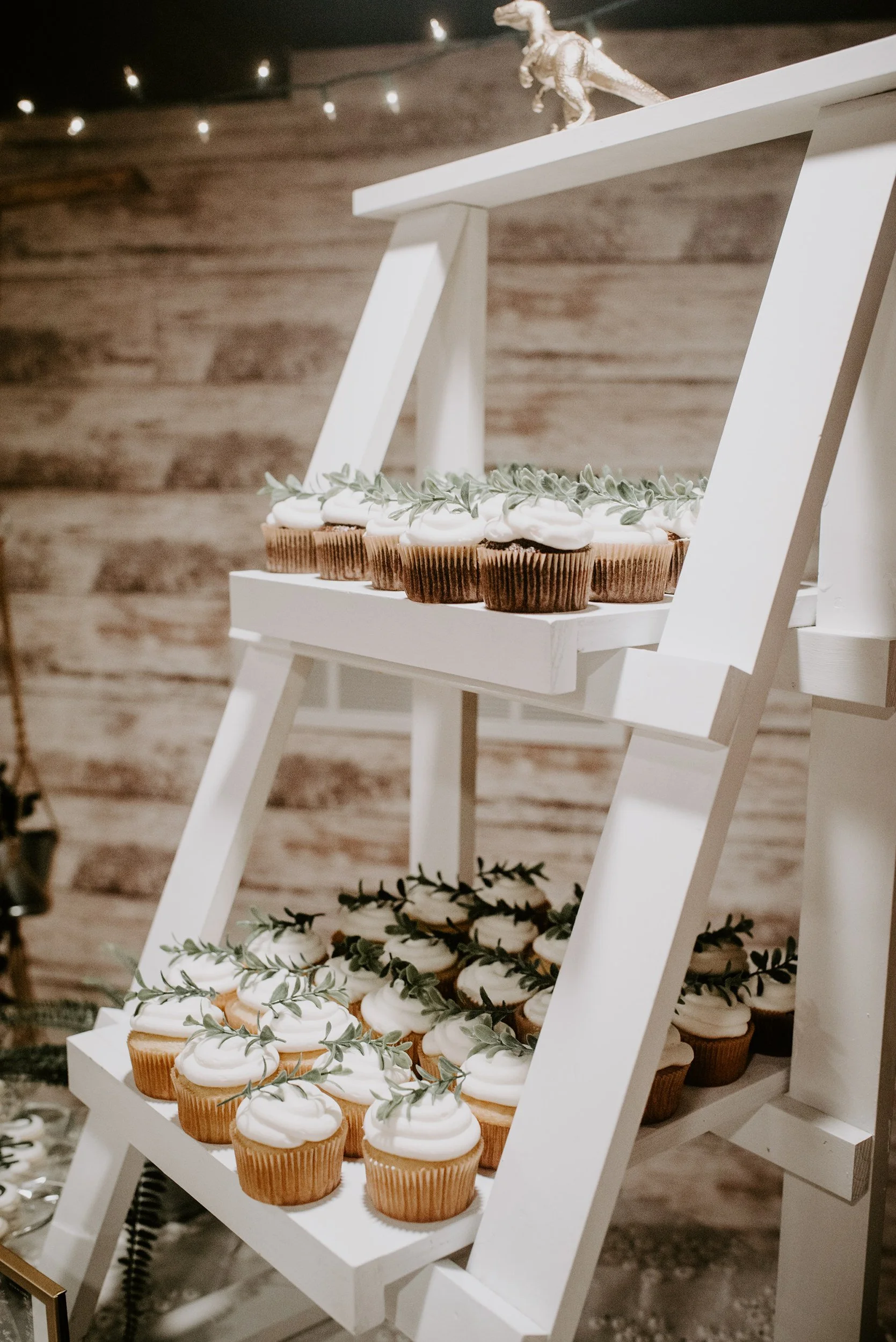 Cupcakes with white frosting and green garnish on a white wooden shelf with a rustic wood wall background.