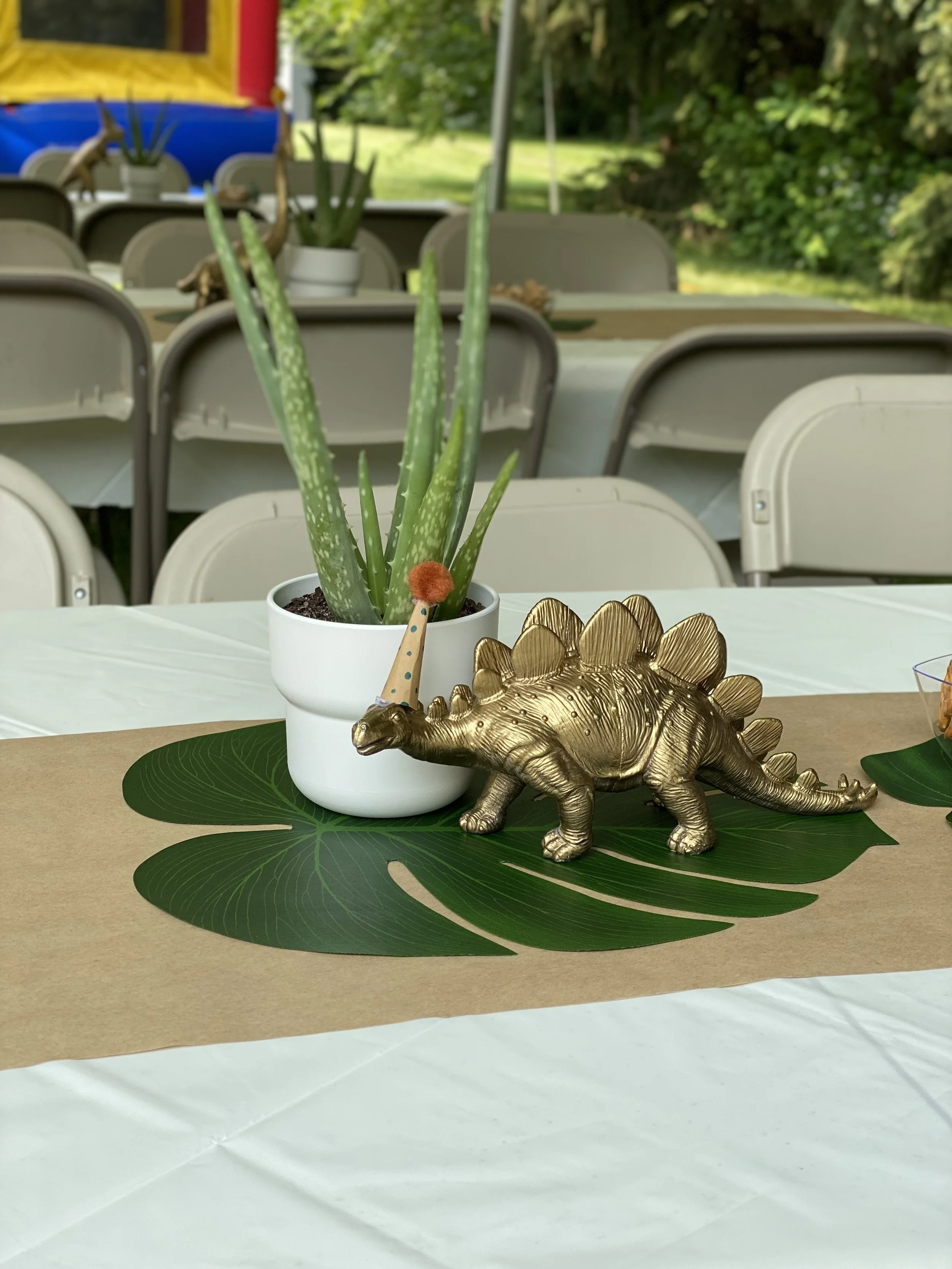 Decorative gold dinosaur figurine and potted aloe vera plant on a Monstera leaf placemat on a table