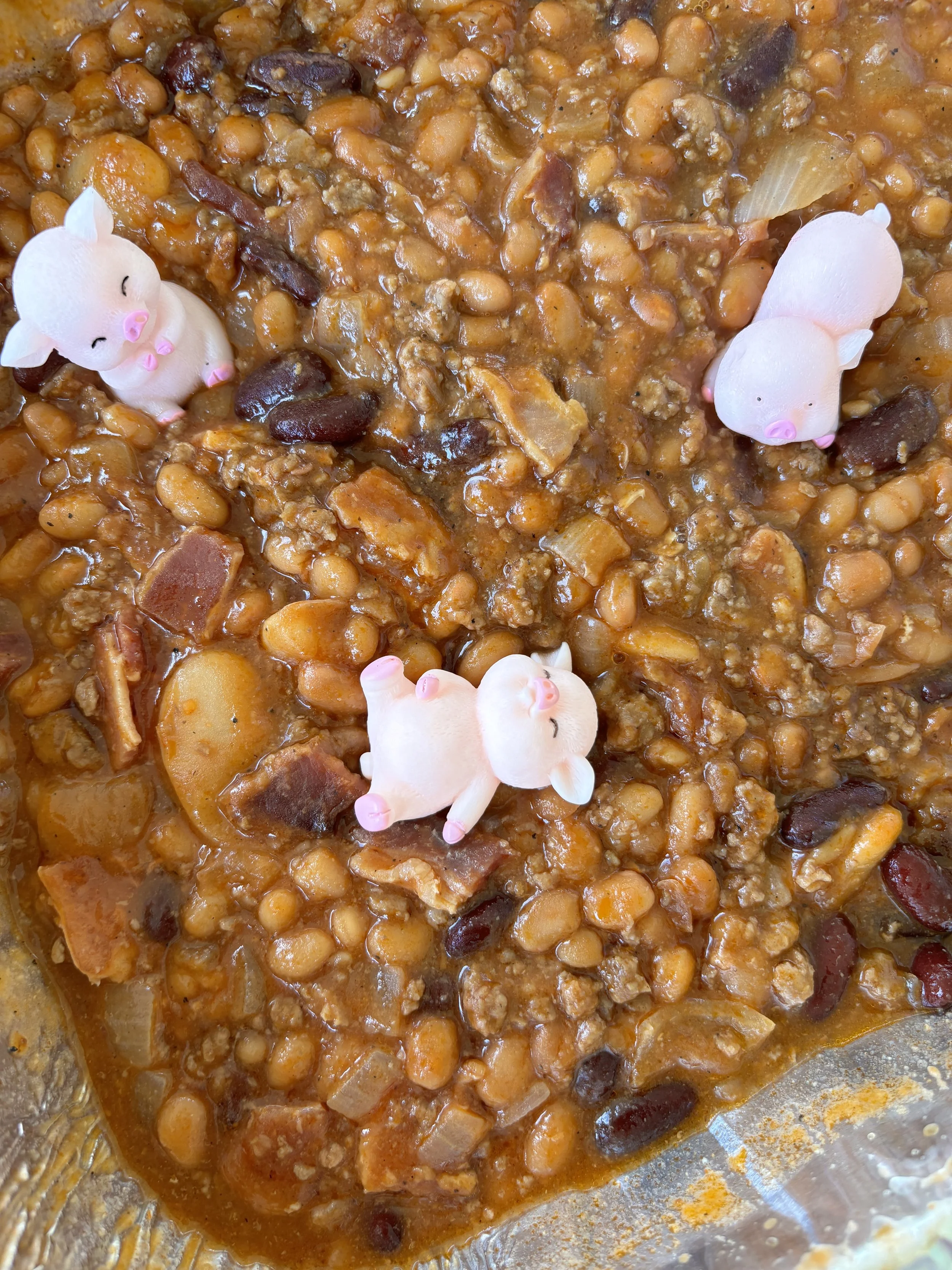 Baked dish with ground meat, beans, and vegetables. Four small pink pig figurines are placed on top as decoration.