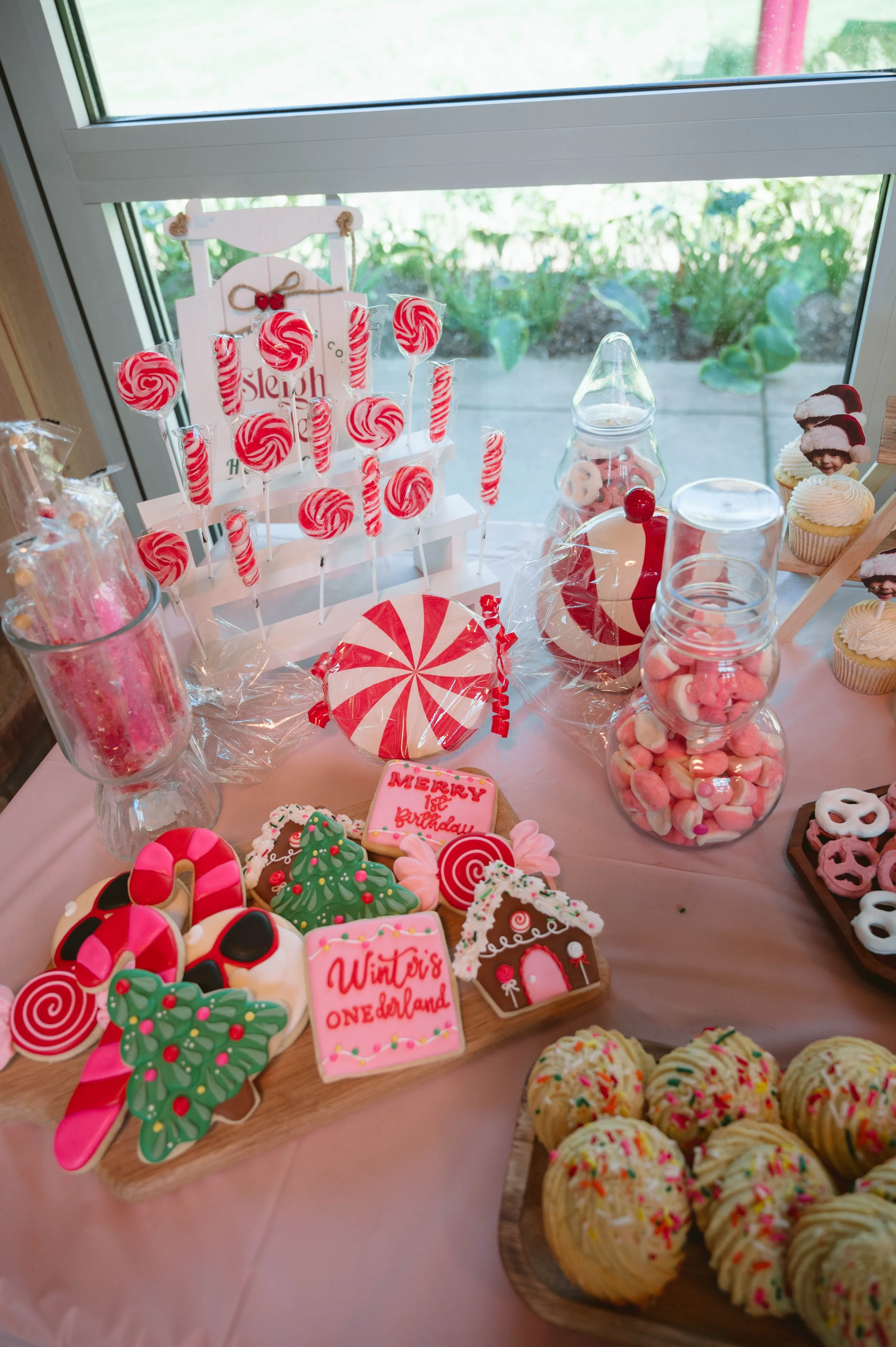 A table decorated for a holiday celebration with Christmas-themed cookies, cupcakes, candies, and decorations, including Christmas trees and gingerbread houses.