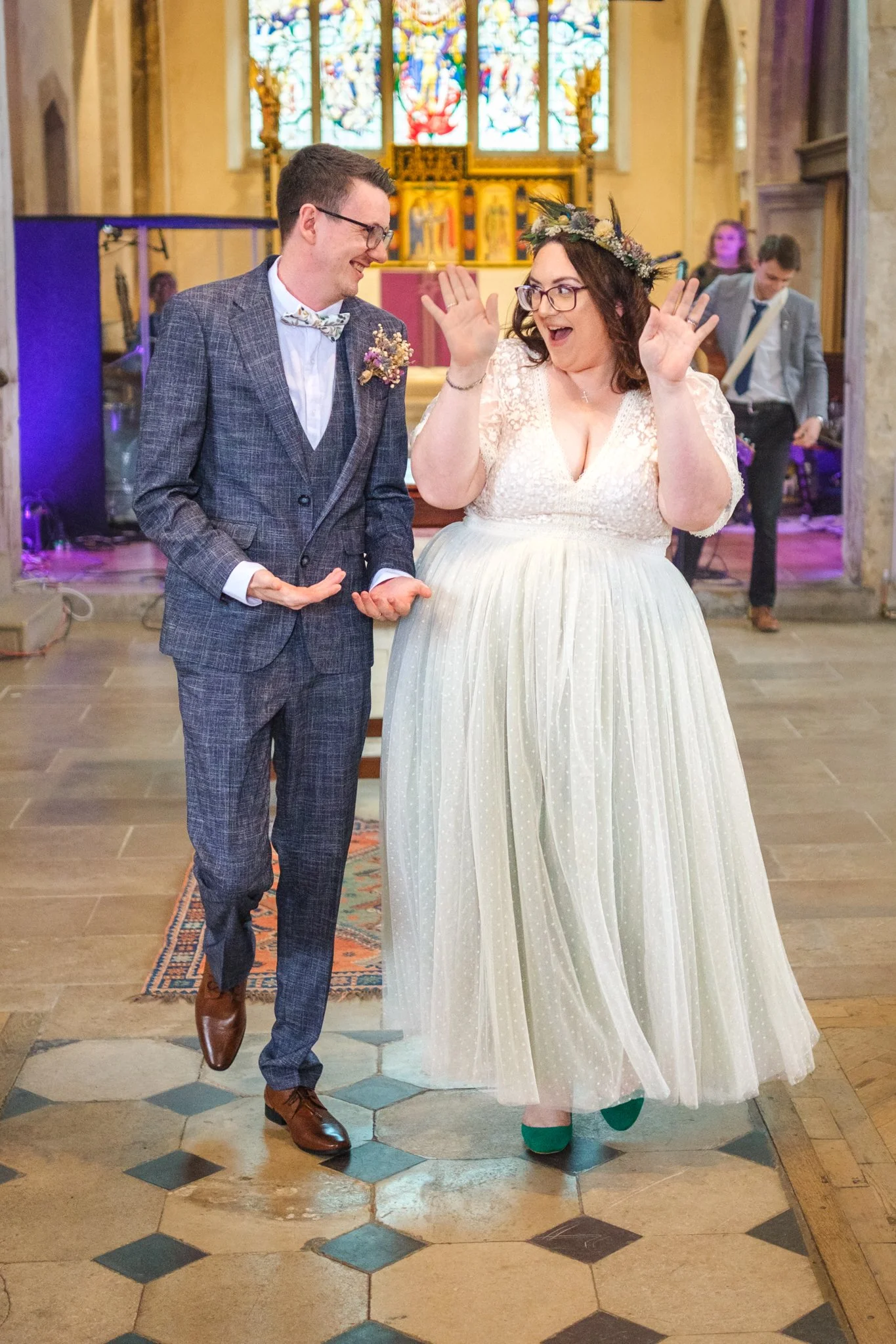 A bride and groom dancing happily inside a church during their wedding ceremony, with a stained glass window in the background.
