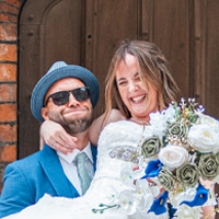 Man and woman smiling, holding a bouquet of flowers, in front of a wooden background.