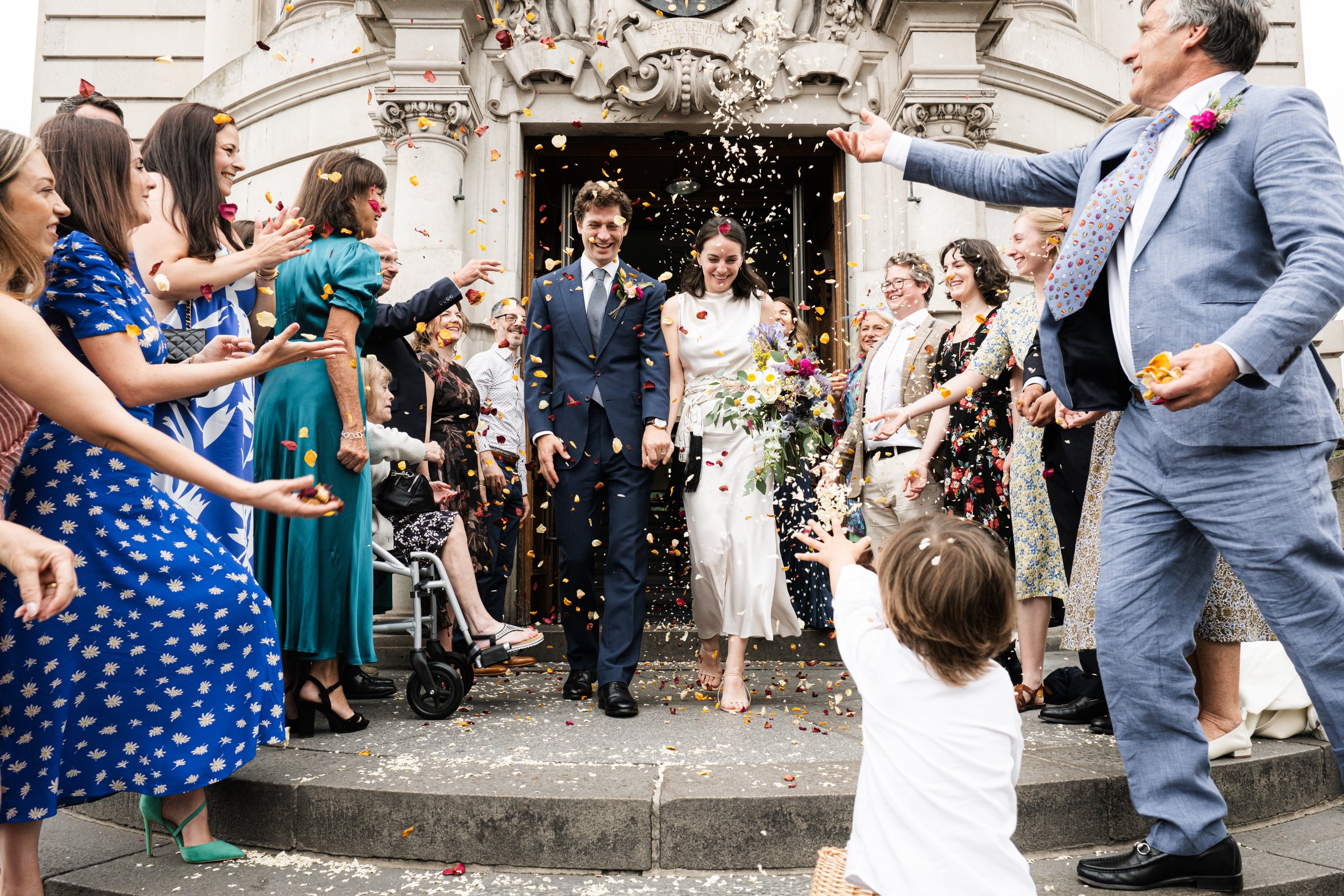 A newlywed couple walking out of a church, surrounded by friends and family throwing flower petals and celebrating.