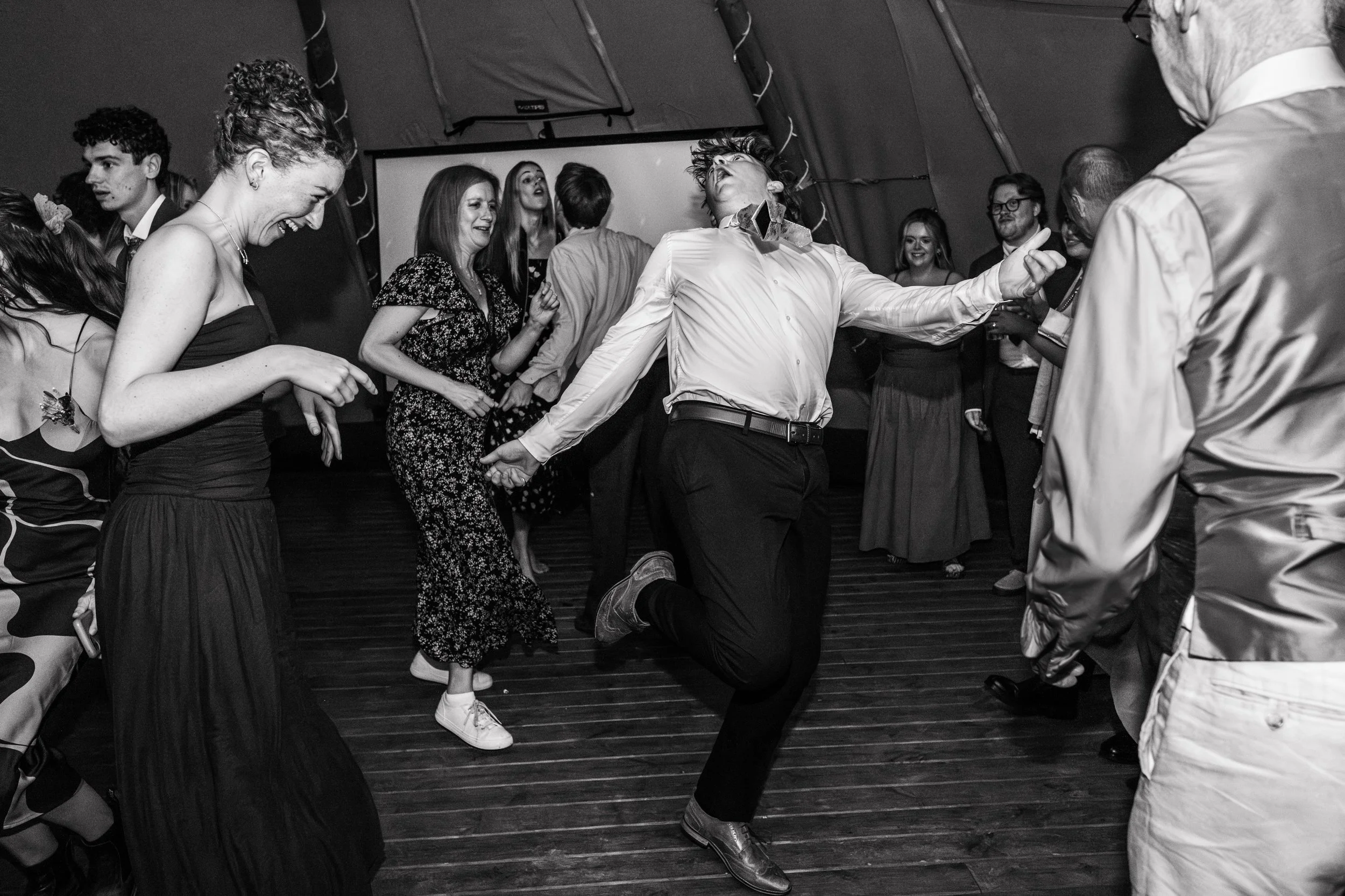 People dancing and enjoying themselves at a lively party or celebration, with a man jumping and others smiling and dancing around him.