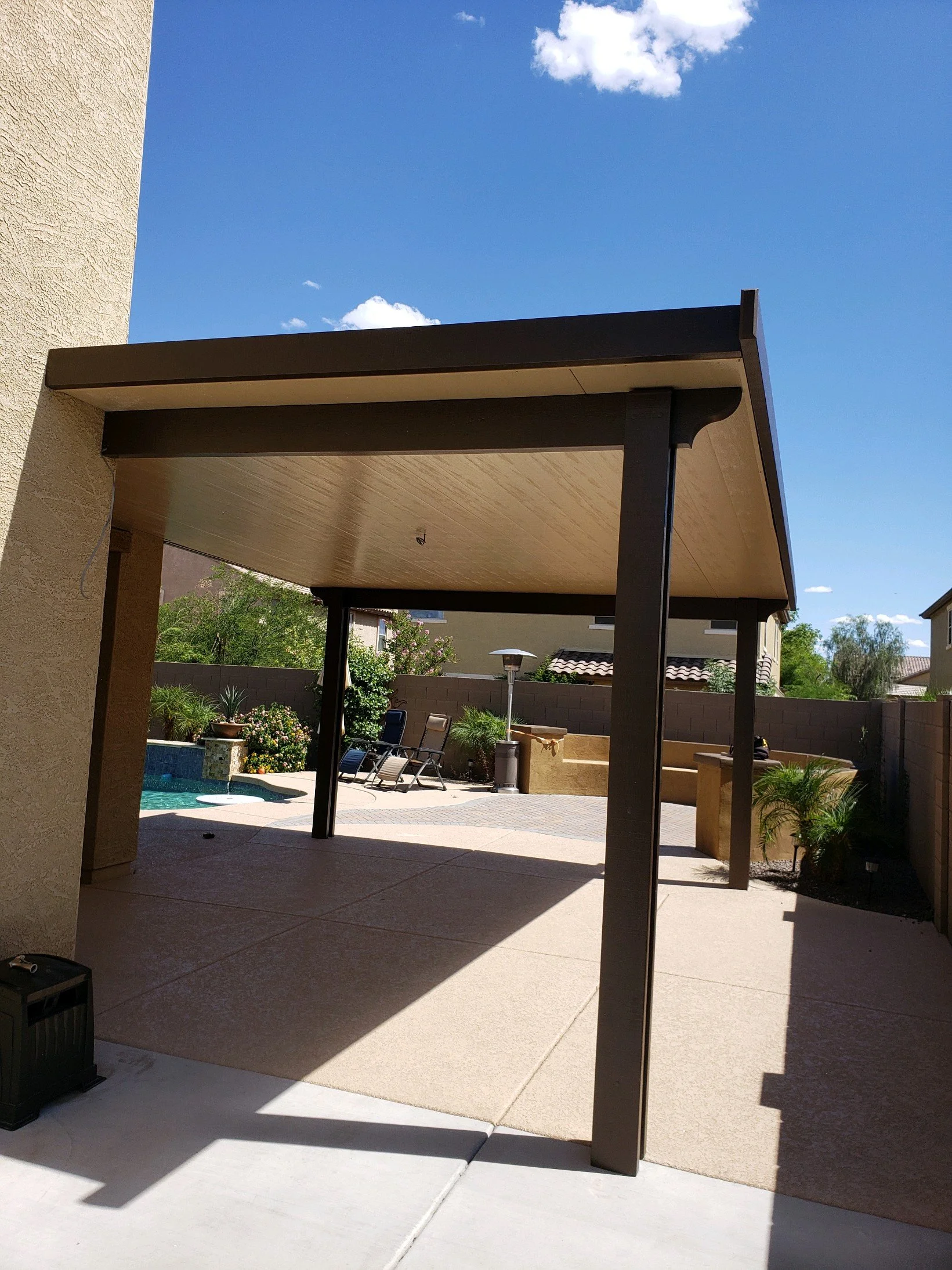 Backyard patio with a covered structure, lounge chairs, a small pool, potted plants, and a clear blue sky.
