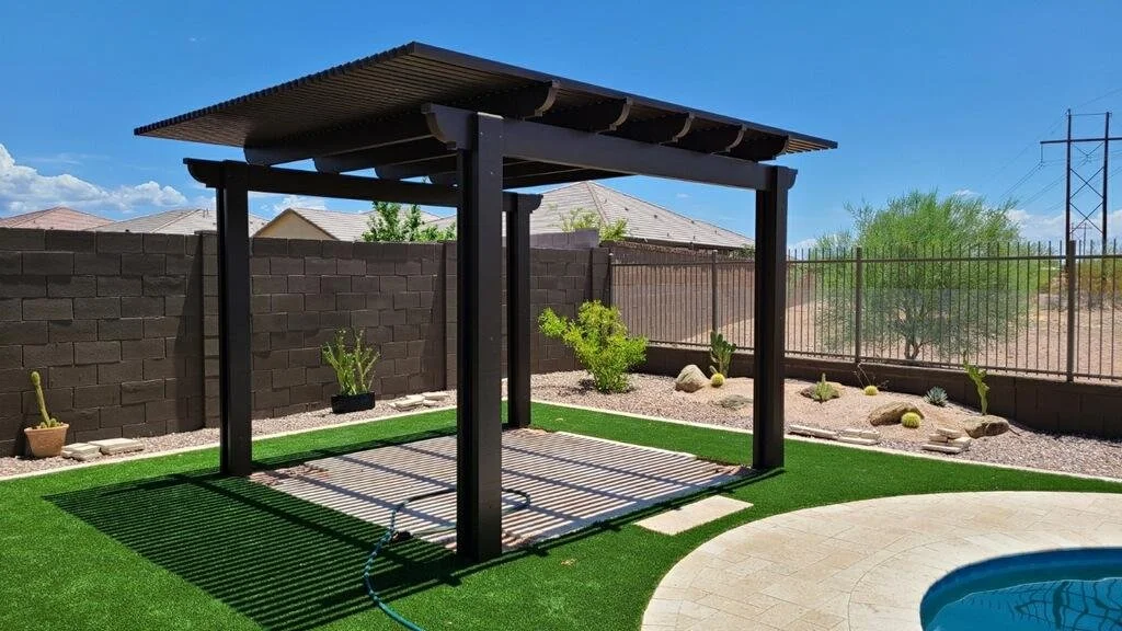 Backyard with artificial grass, a covered wooden patio, potted cacti, desert landscaping, and a swimming pool.