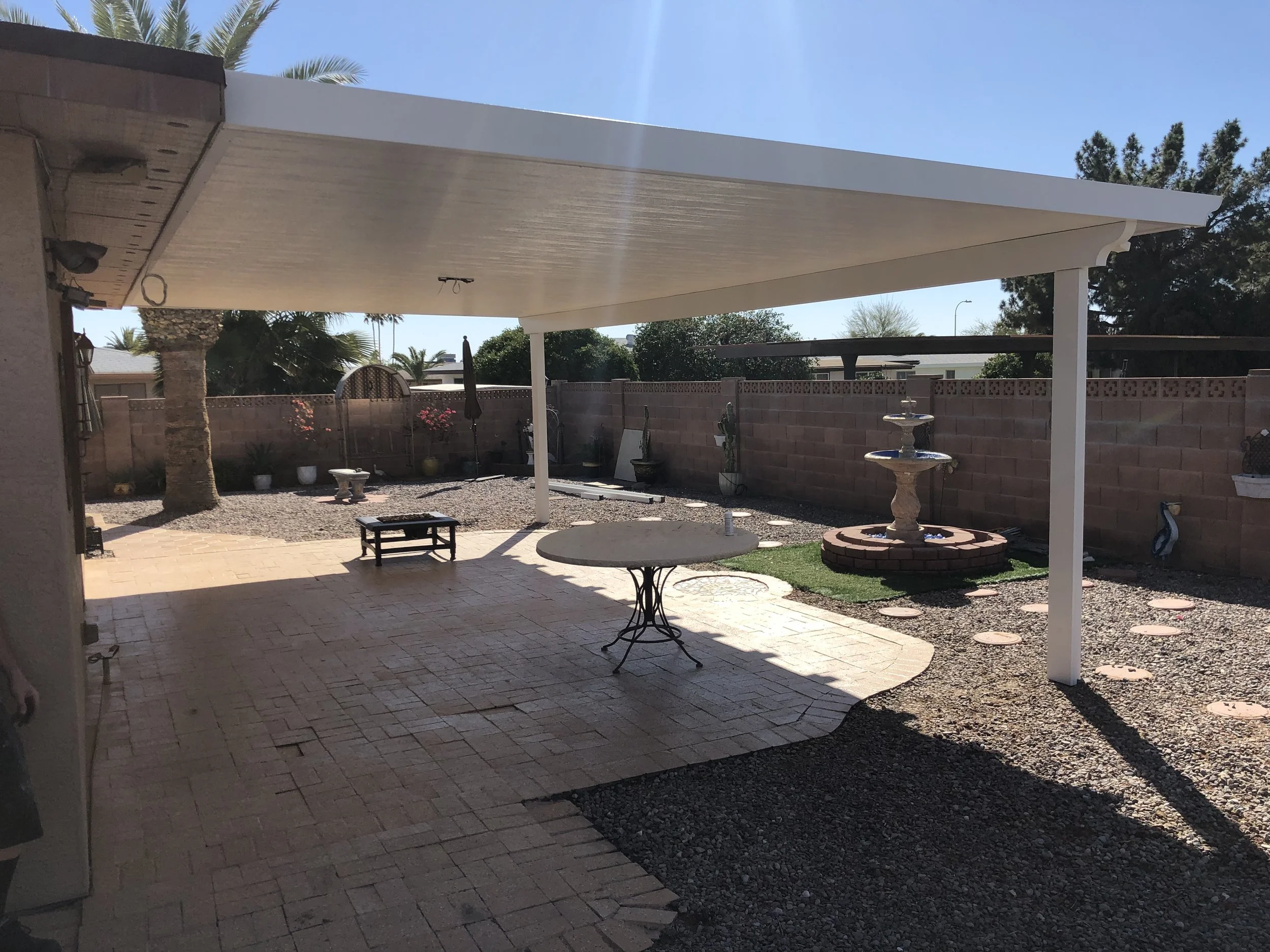 Backyard patio with shaded area, a fountain, potted plants, and a brick wall fence.