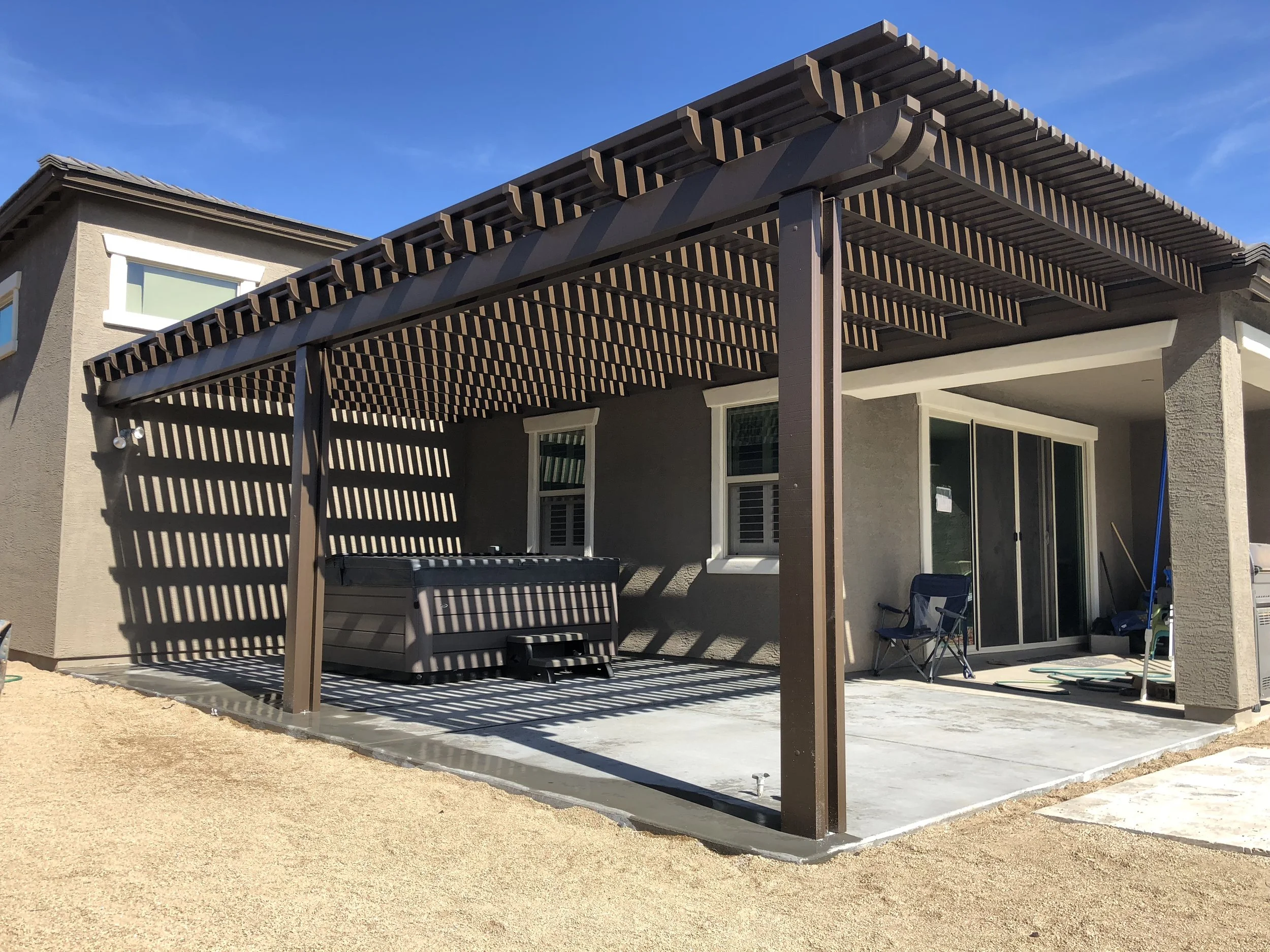 Backyard patio with a wooden pergola, a hot tub, patio chairs, and a sliding glass door leading into the house.