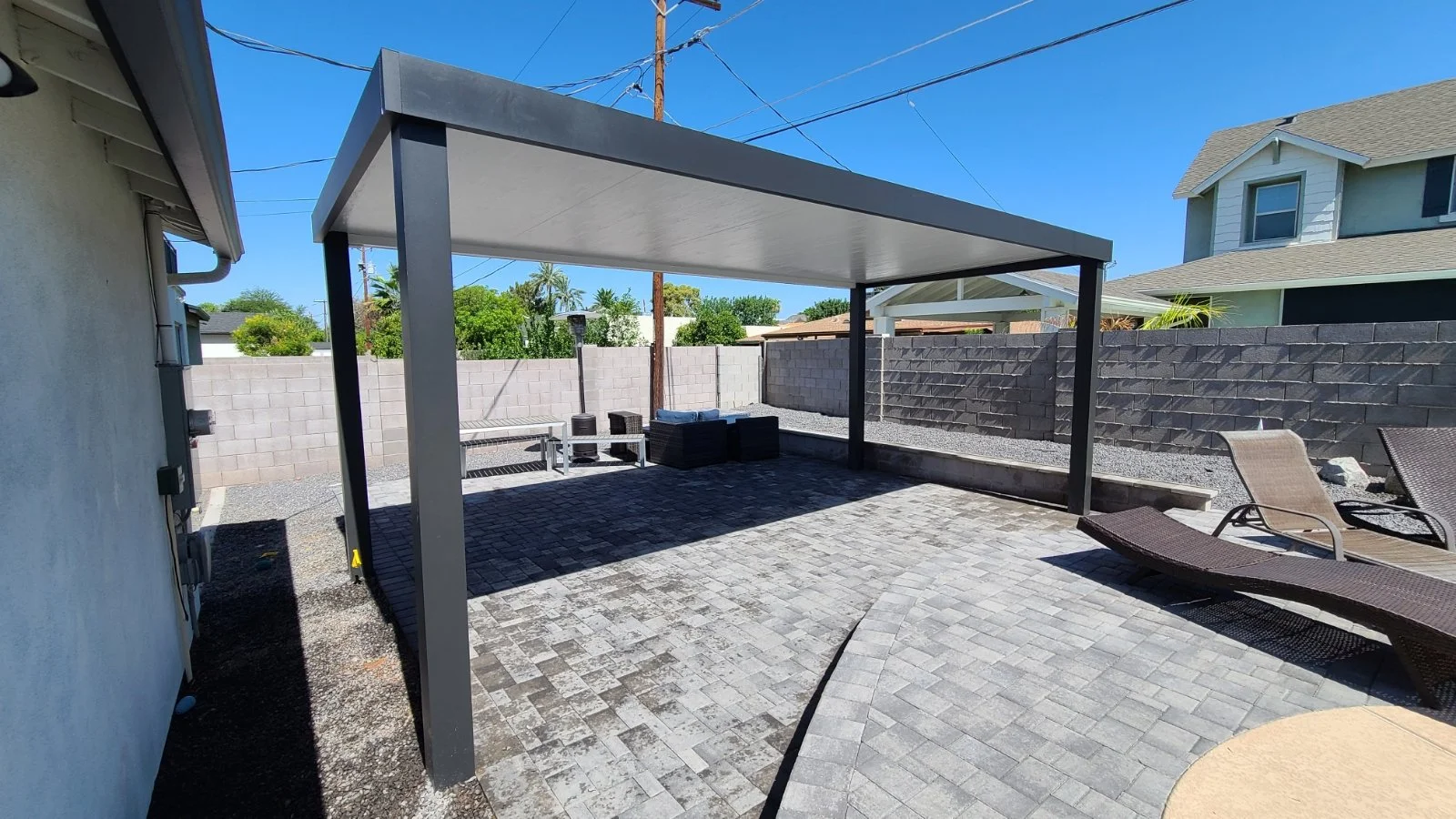 Backyard patio with a shaded gazebo, lounge chairs, a stone pathway, a brick wall, and a neighboring house.