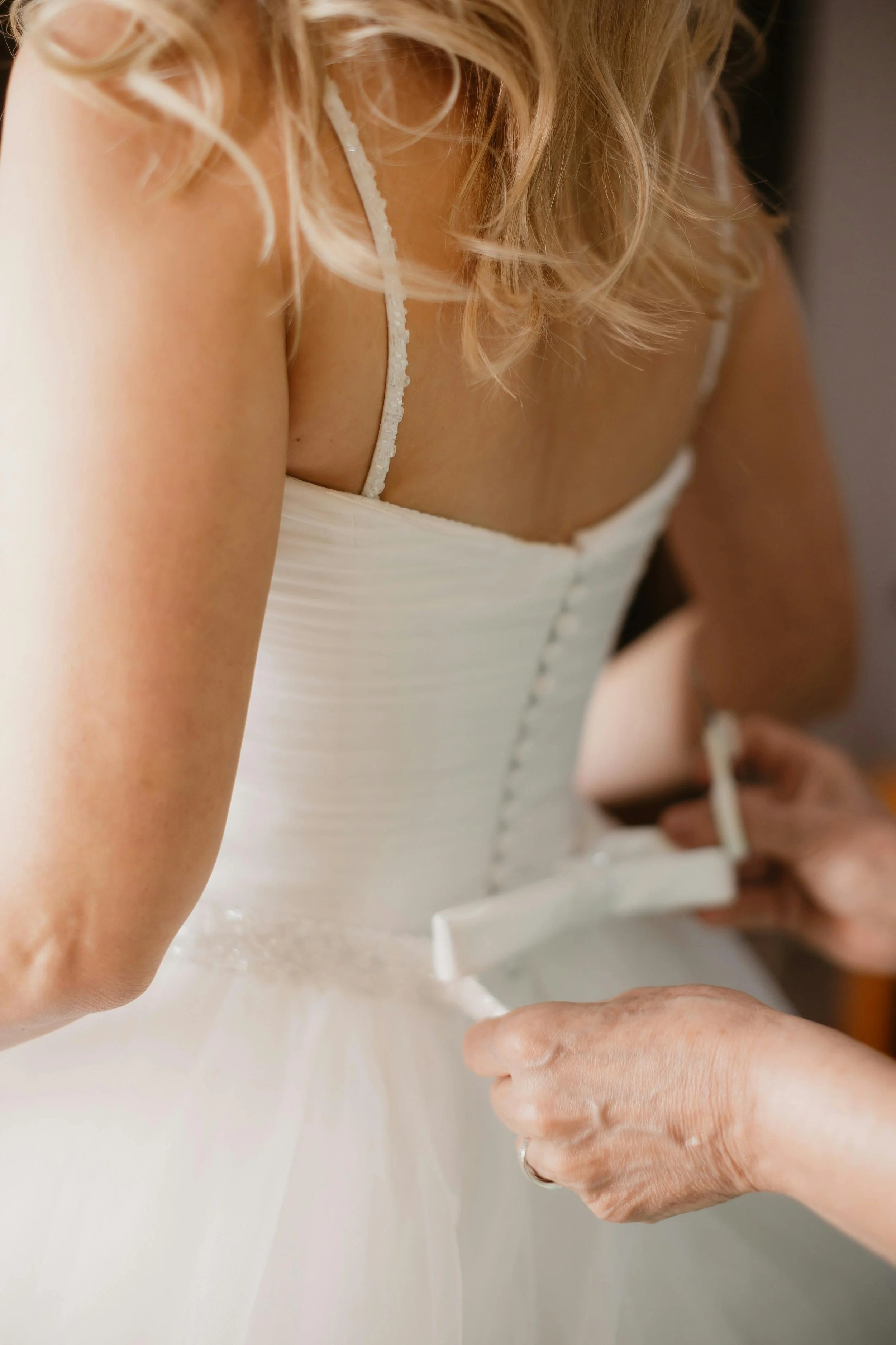 A newlywed couple sharing a kiss in front of a lush green wall of ivy. The groom is dressed in a black suit, the bride is wearing a white wedding gown and holding a bouquet of flowers.