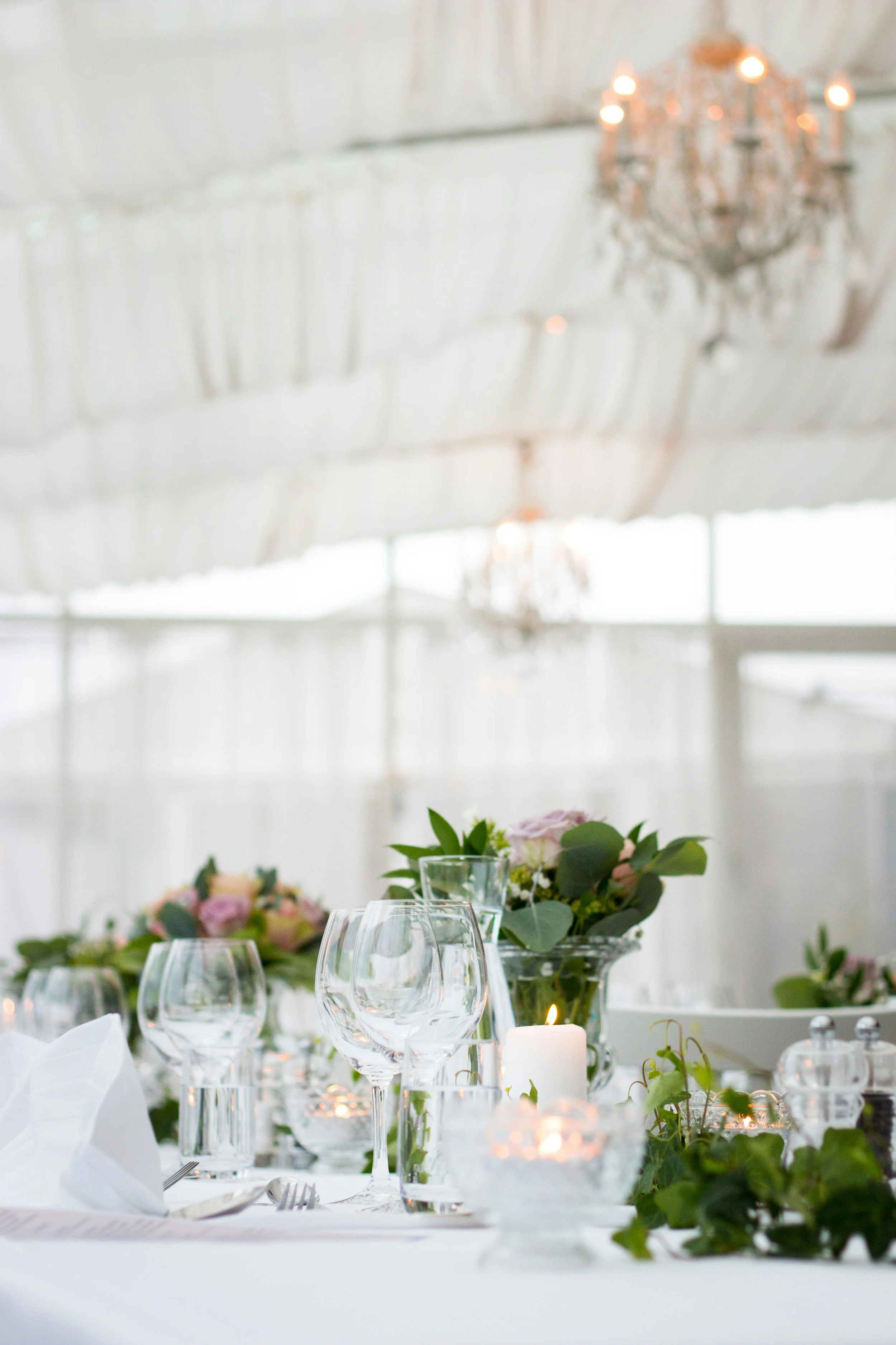 Elegant banquet table with wine glasses, candles, and floral arrangements in a bright, airy venue with chandeliers.