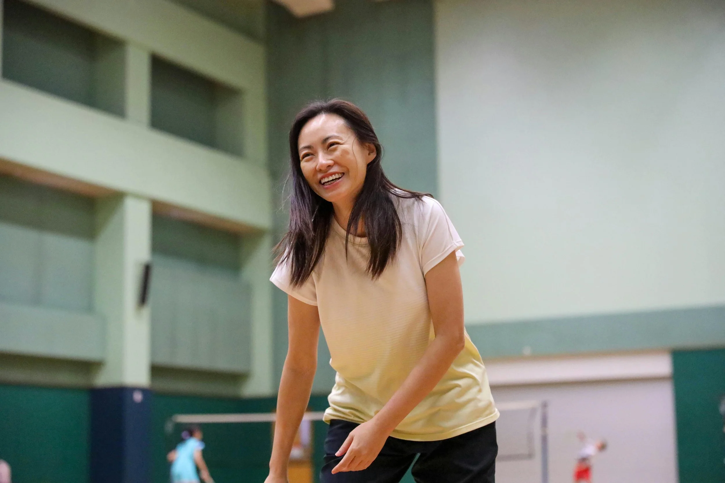 Woman laughing and playing badminton in an indoor court.