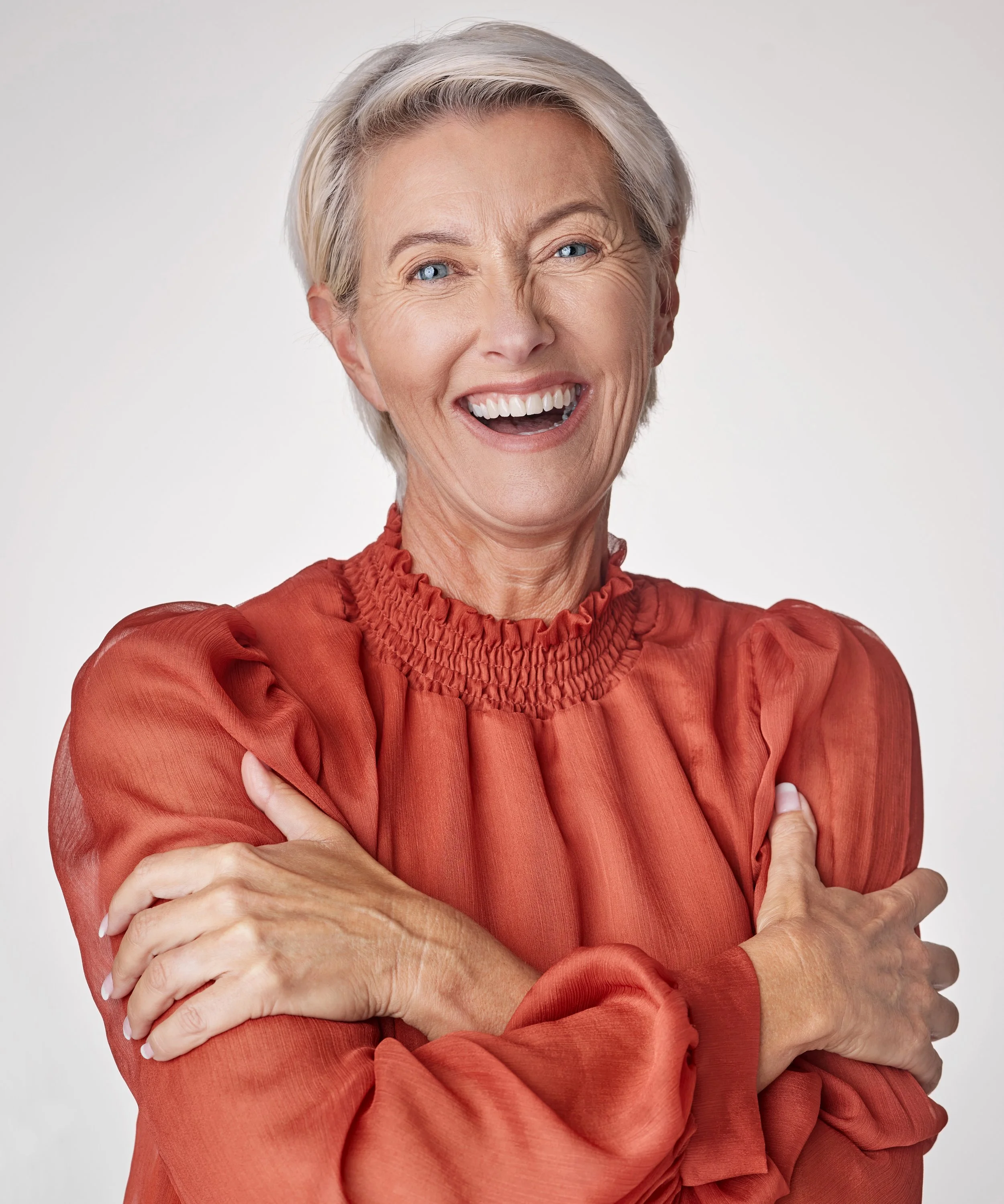 Headshot of woman in coral colour blouse with arms folded across chest