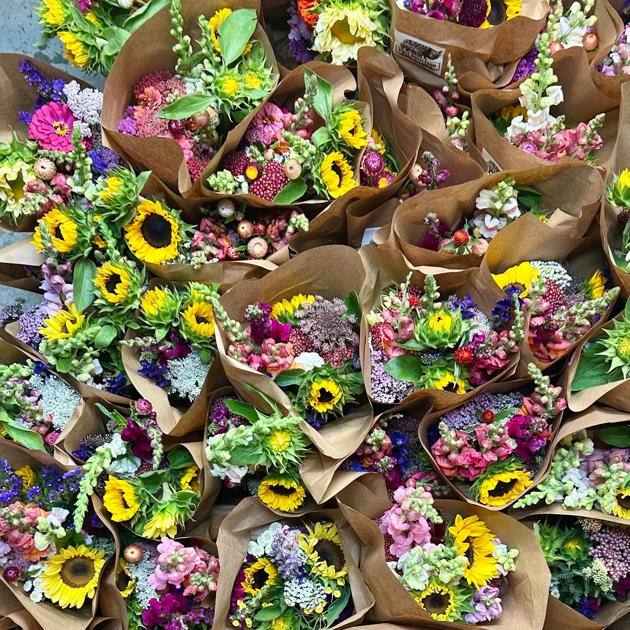 Multiple bouquets of multicolored flowers wrapped in brown paper.