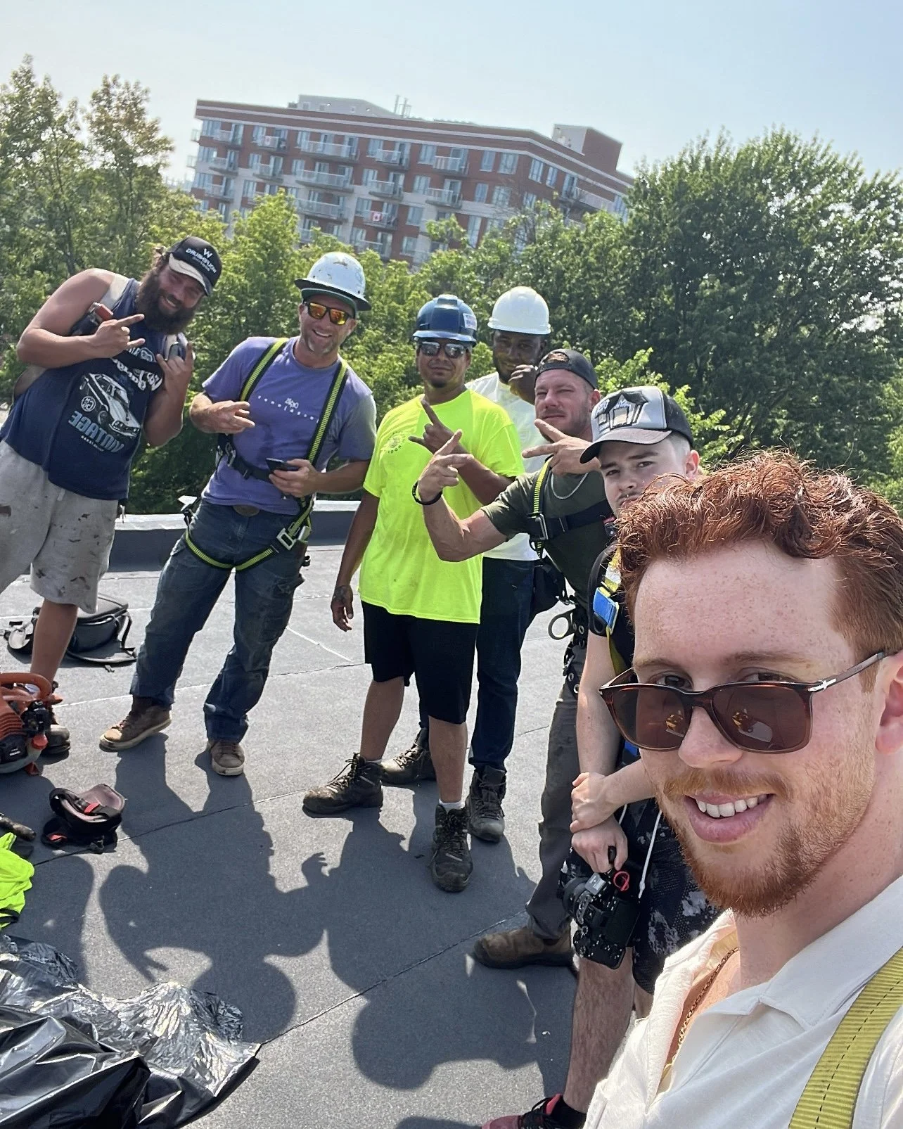 Group of people outdoors, some wearing helmets and harnesses, taking a selfie on a sunny day with a building in the background.