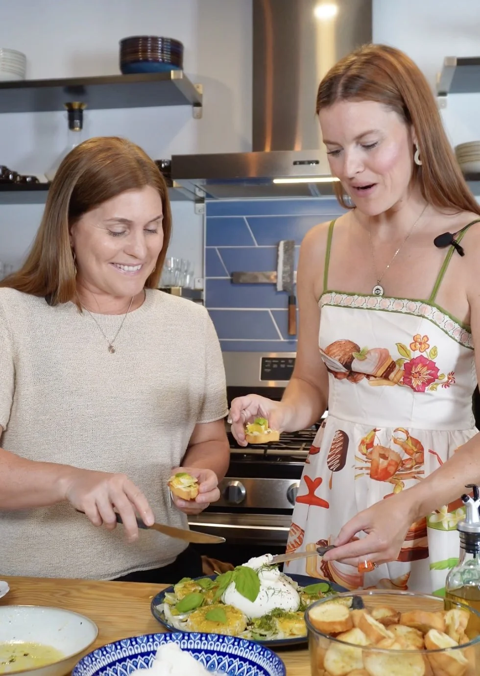 Two women preparing food together in a kitchen, smiling and serving dishes onto plates.