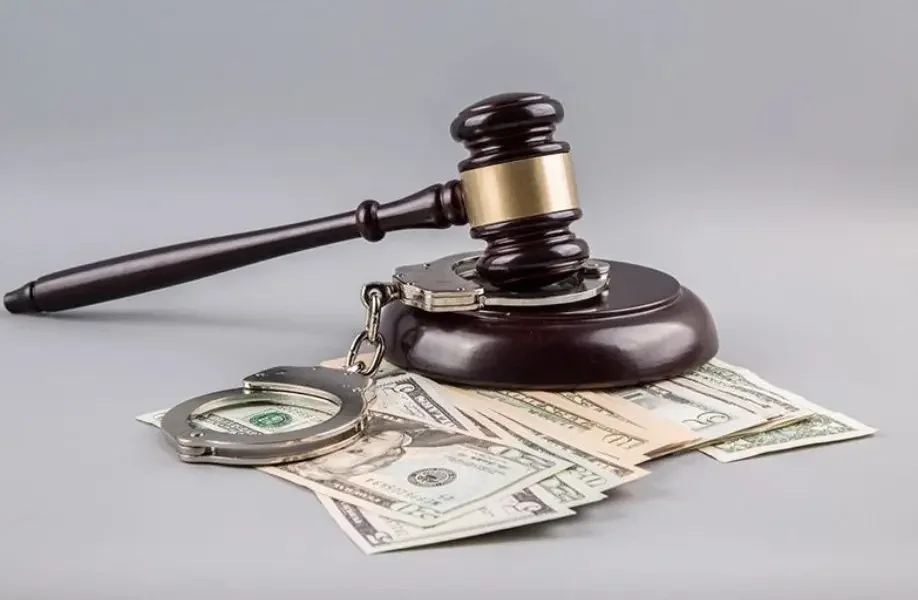 Un mazo de juez, unas manillas y dinero en billetes sobre una superficie gris.