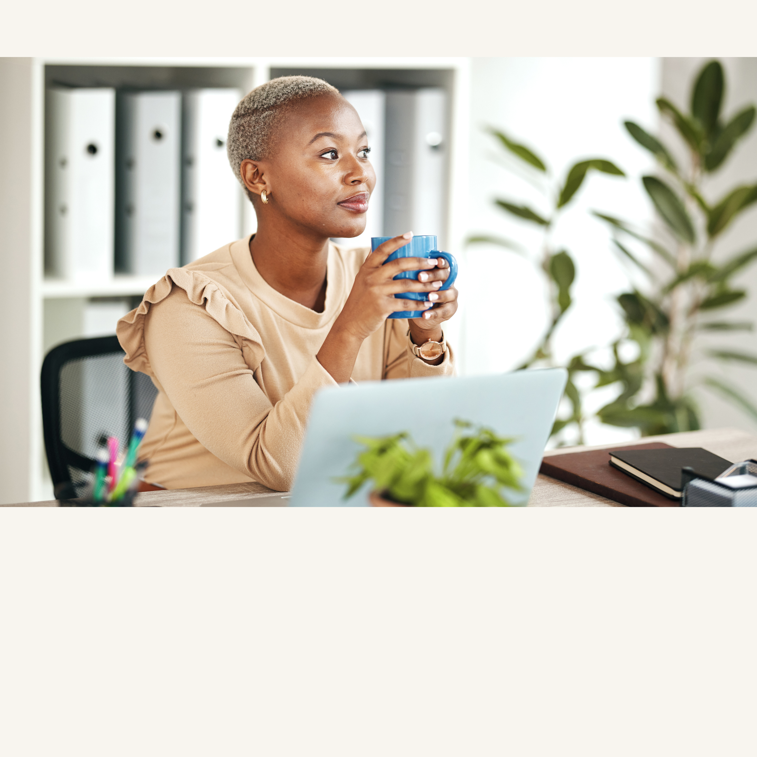 Black woman with a coffee mug at her desk, looking away in thought