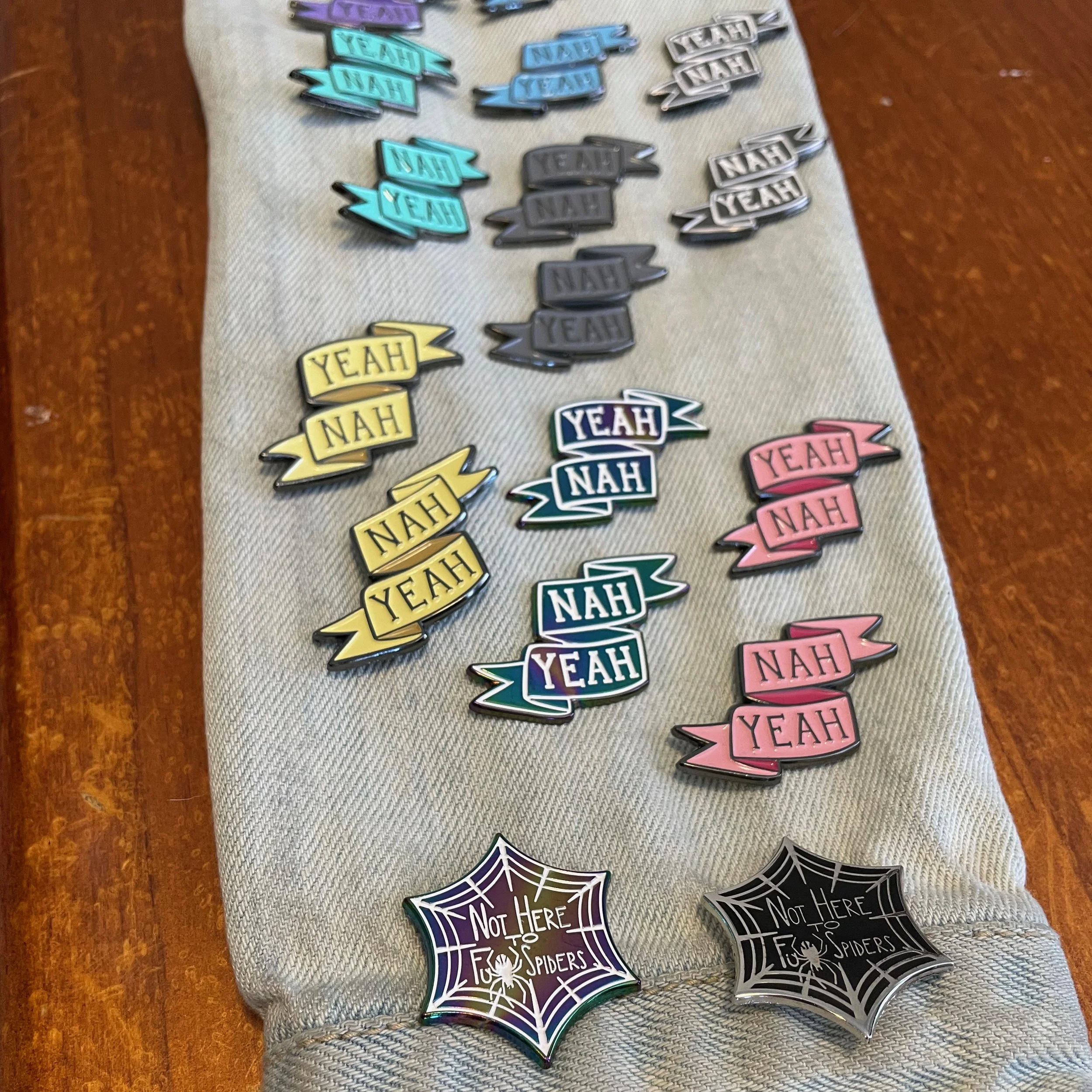 Photograph of Yeah Nah, Nah Yeah, and Not Here to F- Spiders enamels pins, in various colors, on a denim jacket sleeve.