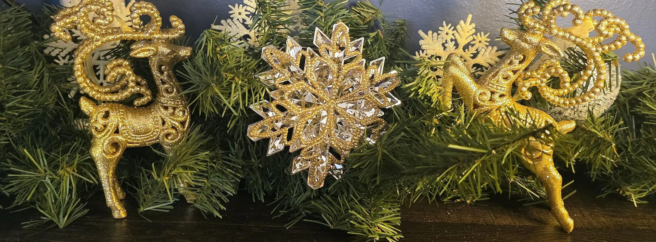 A close-up of festive holiday garland decorated with gold reindeer and a sparkling gold snowflake ornament, styled on a dark wood surface.