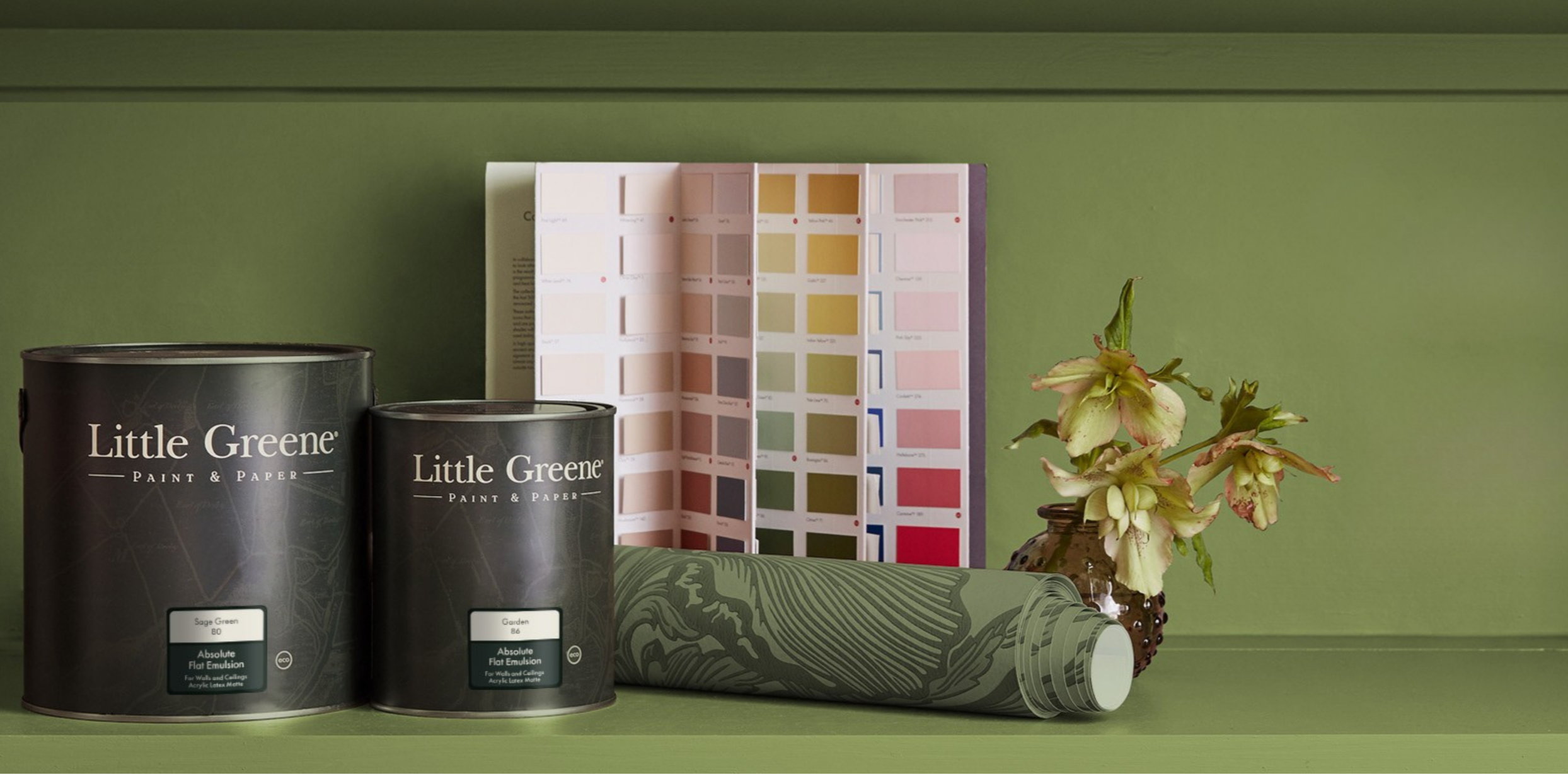 Paint sample cans labeled Little Greene, color swatches, a wallpaper sample, and a vase with flowers set against a green wall.
