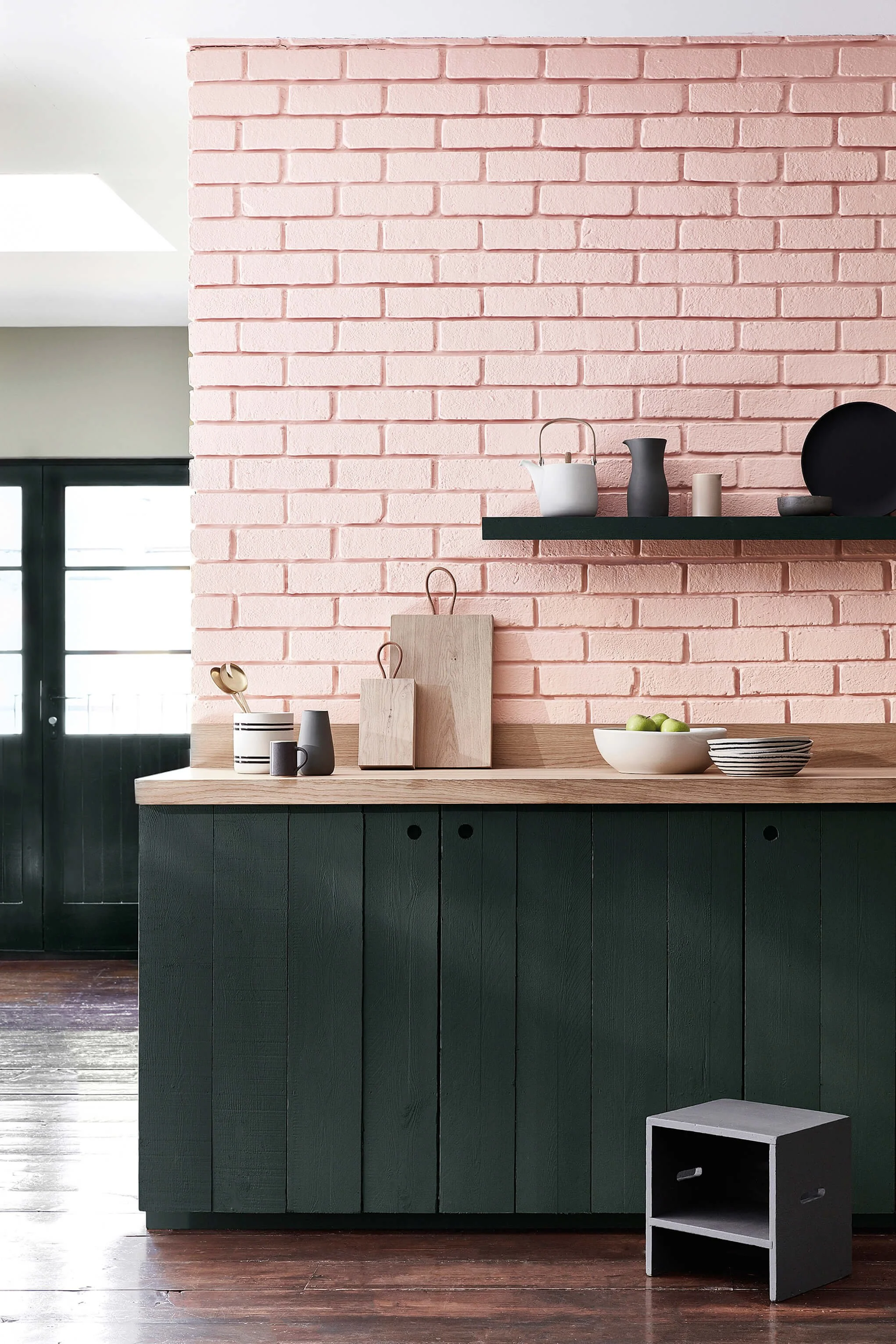 Kitchen with pink brick wall, green cabinetry, wooden countertop, black and white decor, and a small black side table.