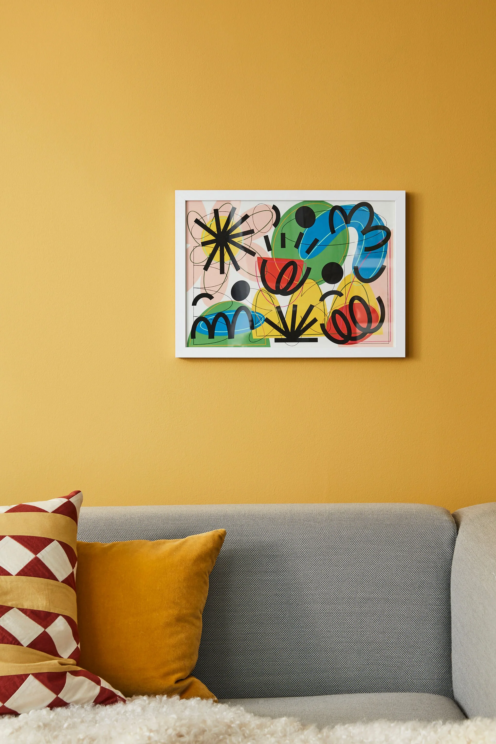 Colorful abstract art on a wall with a yellow background, a white frame, and various colored shapes and lines.