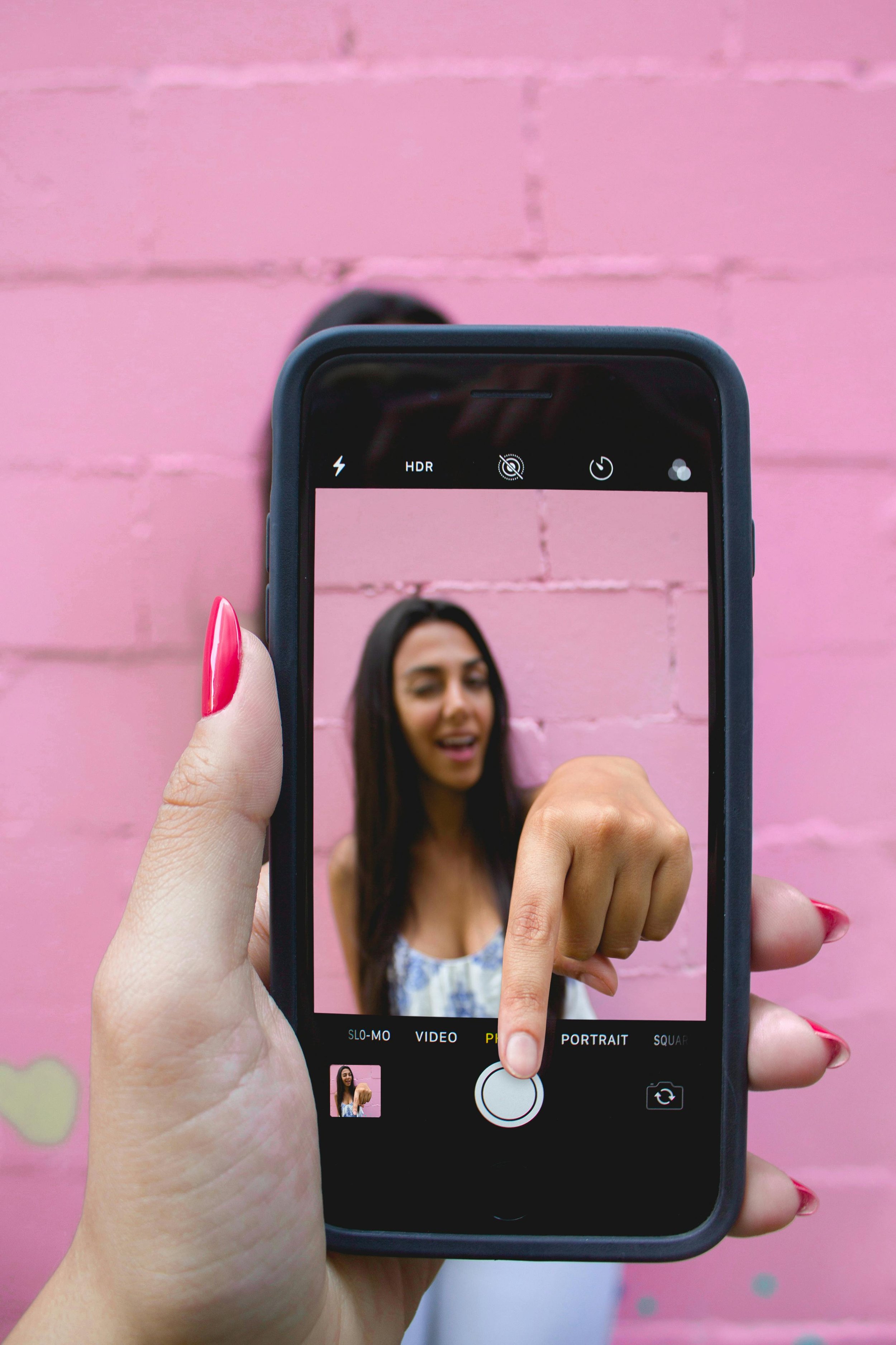 Hand holding phone taking picture of a girl who is pressing the photo button