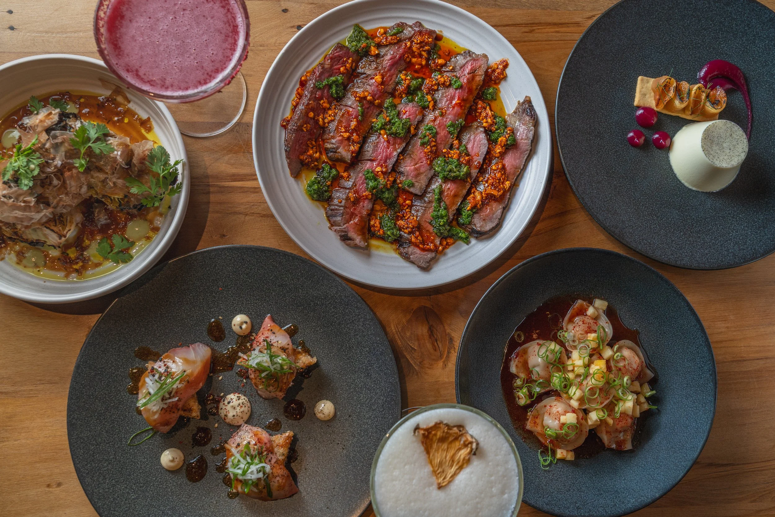 Modern house with wooden exterior and stone steps leading to a terrace, set against a mountainous landscape, with grassy plants around.