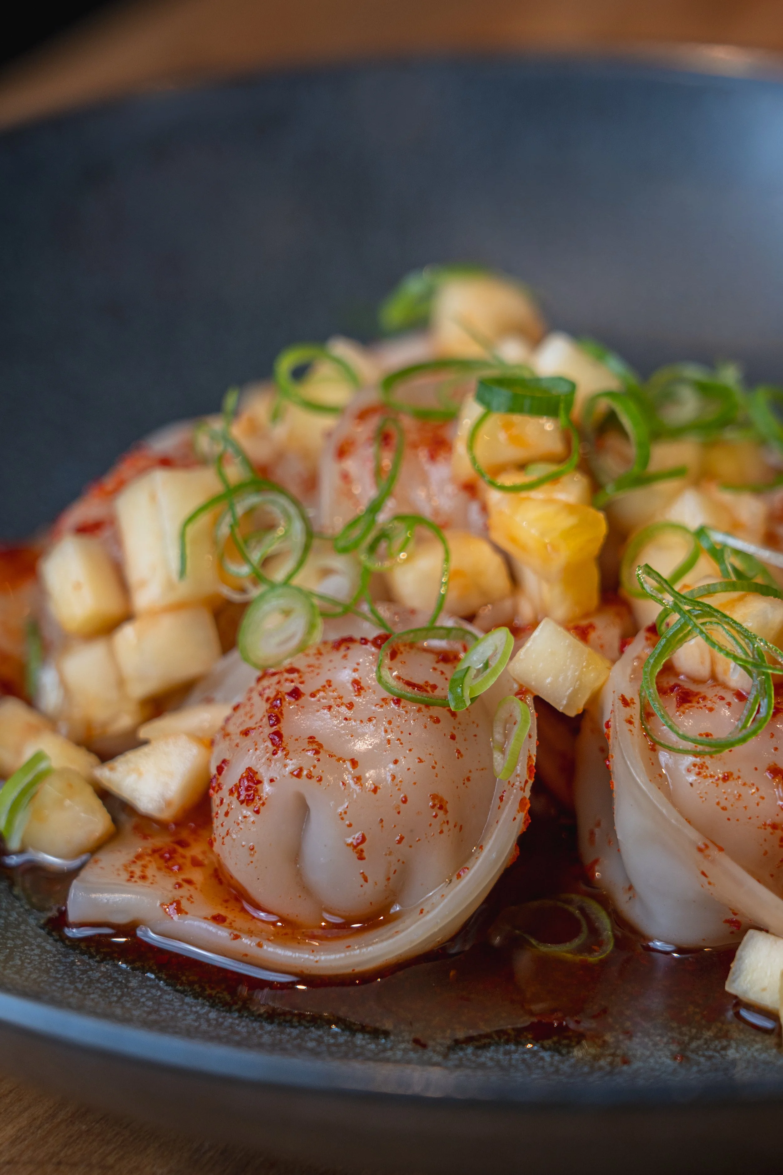 Close-up of a dish with poached eggs, diced potatoes, sliced green onions, and red chili flakes in a skillet.